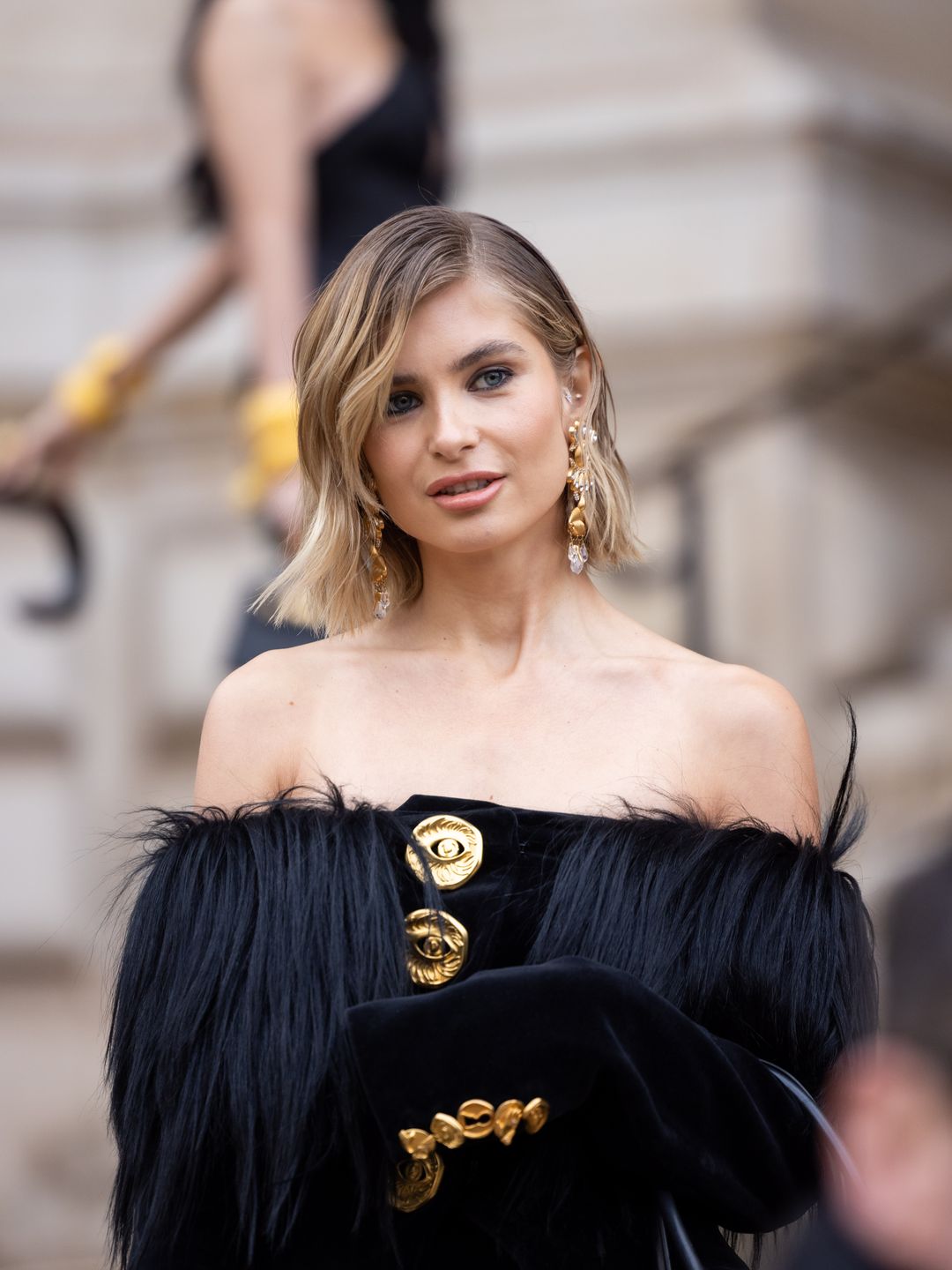 Influencer Xenia Adonts spotted outside the Schiaparelli Haute Couture Spring/Summer 2024 show  wearing an off the shoulder black gown and bob style haircut 