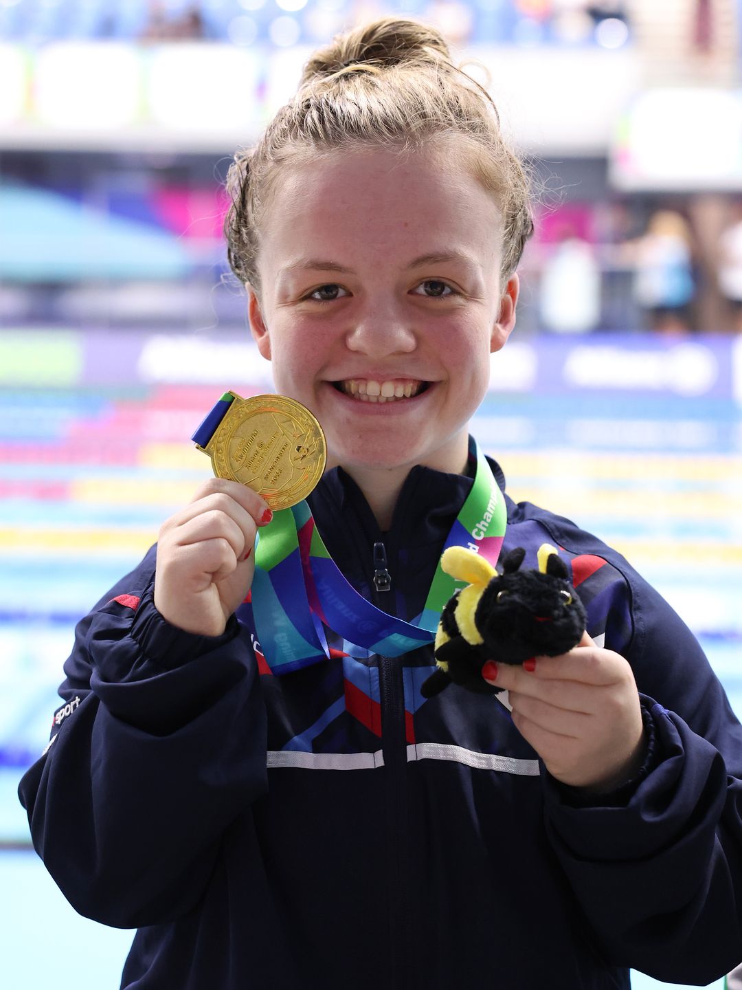 Maisie Summers-Newton holding a gold medal and a plush bumblebee