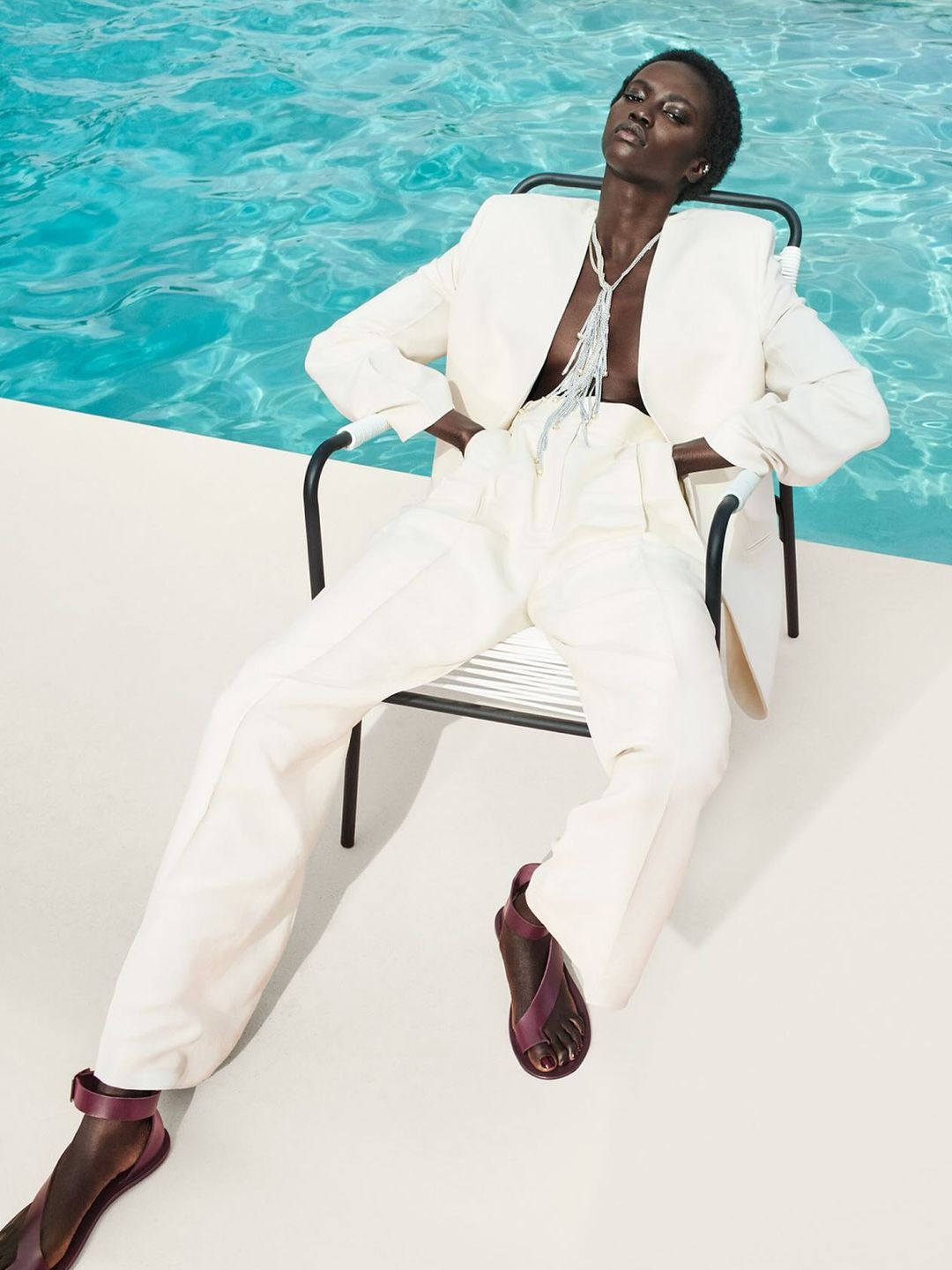 A model poses in a white tailored suit by a pool 