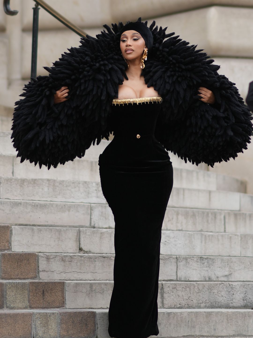 Cardi B wearing a black fitted dress and feathered cape