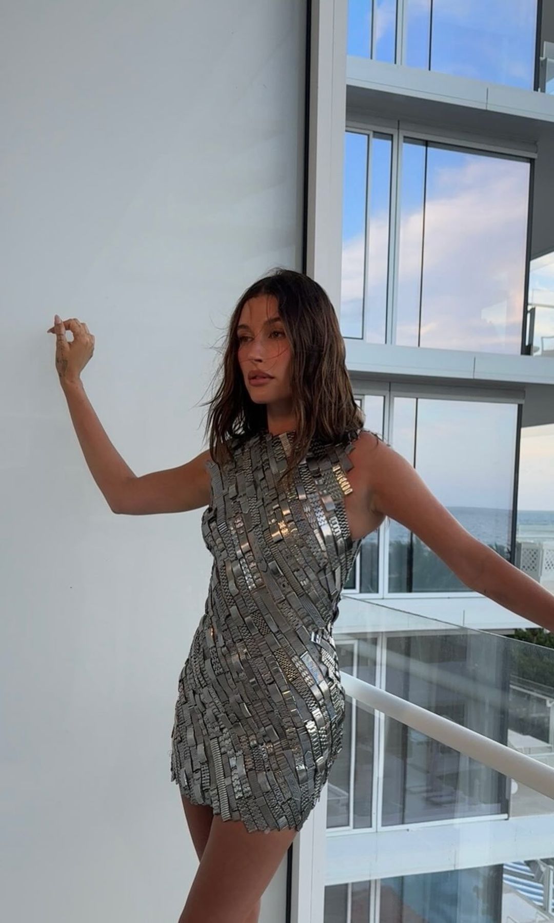 Hailey Bieber poses for a photo on a balcony in a silver mini dress made from old watch straps