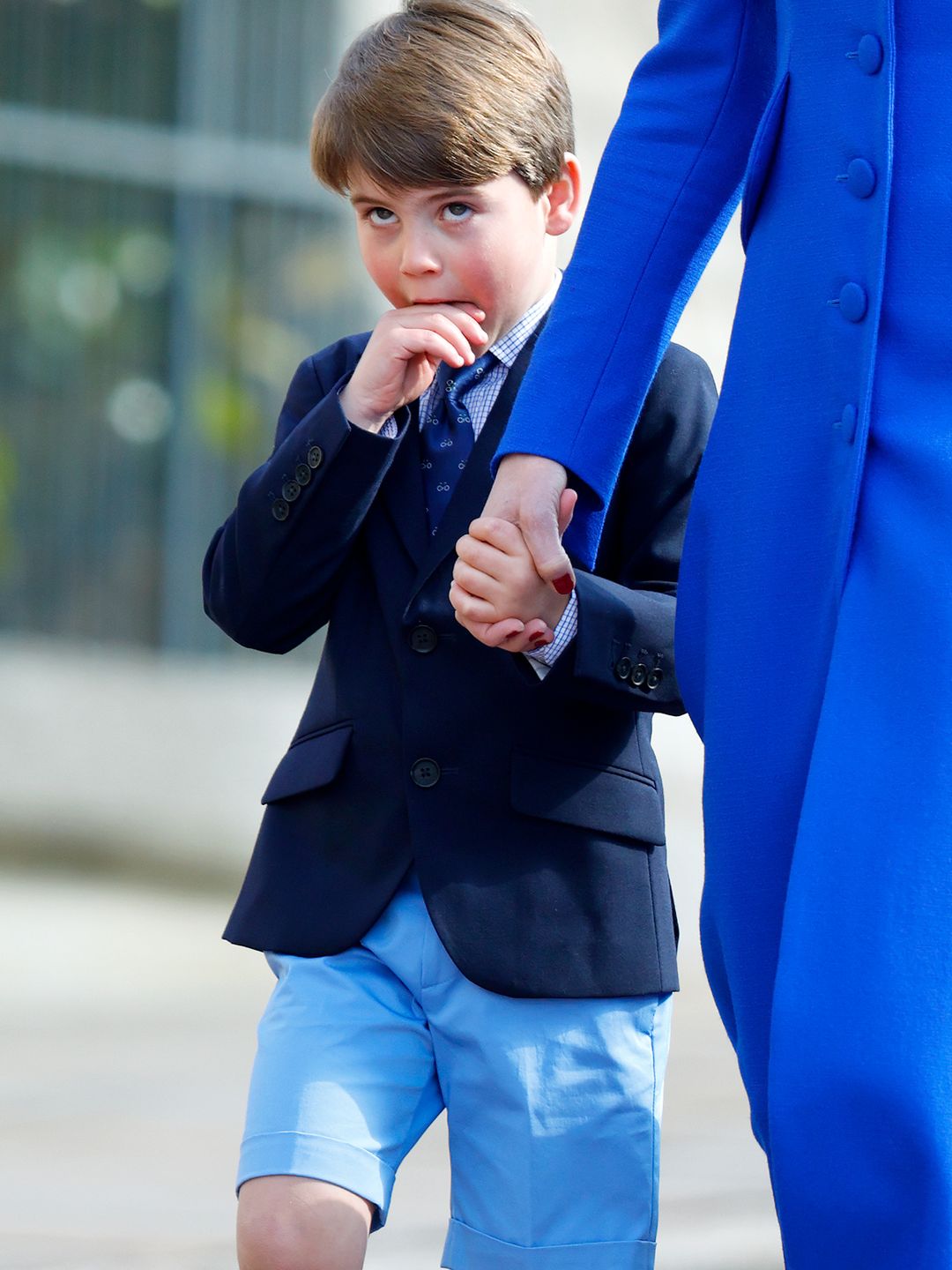 Prince Louis biting one hand as he holds Kate's hand