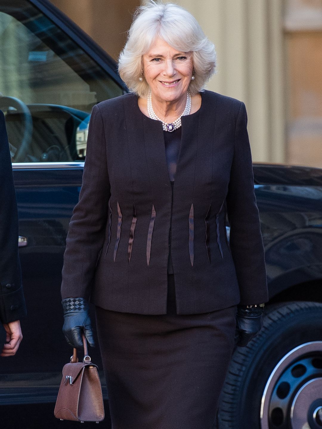 Rainha Camilla usando saia preta coordenada e bolsa Moynat 