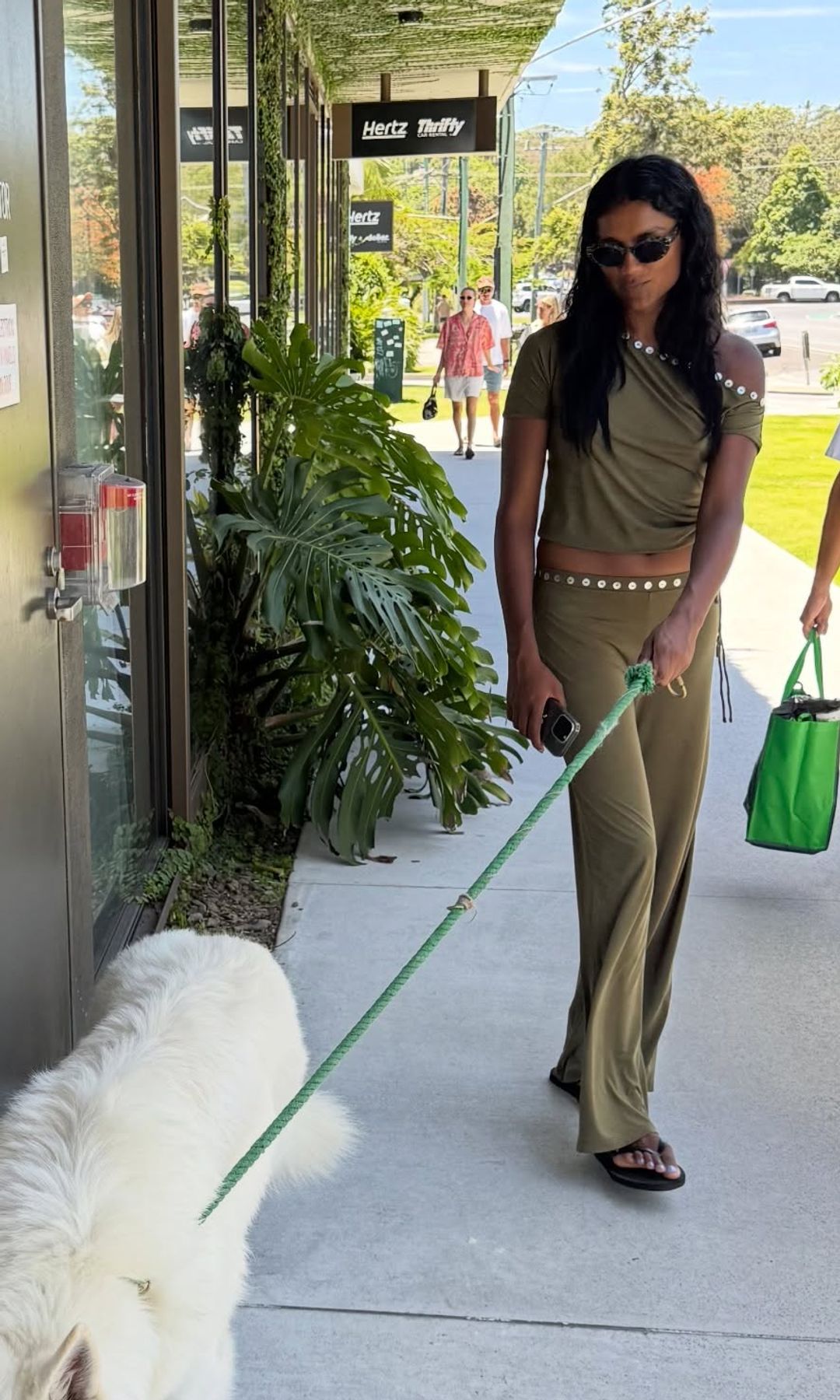 Simone Ashley walks a white dog in LA wearing a green trouser and top combo