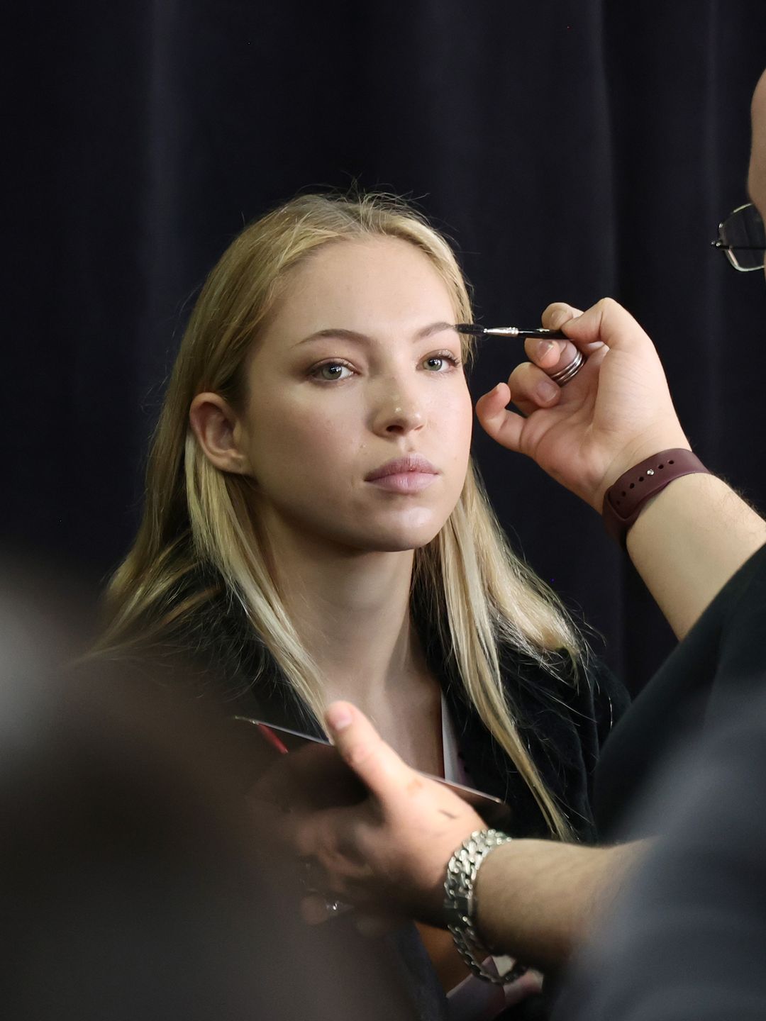 Lila Moss sat still as her makeup artist meticulously shaped her brows. The serious expression on her face highlighted the focus and precision needed to achieve runway-ready perfection behind the scenes.