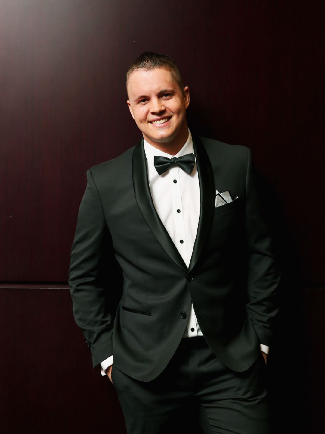 Johnny Ruffo wearing a tuxedo and smiling. 