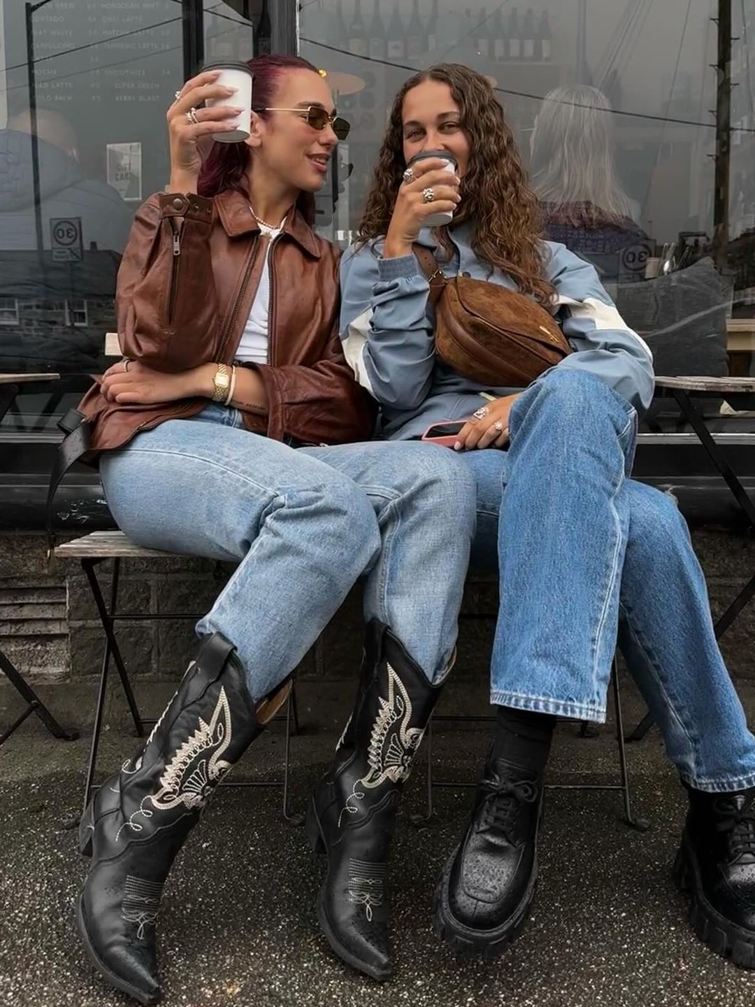 Dua Lipa and Sarah Lysander pose on a bench with coffees