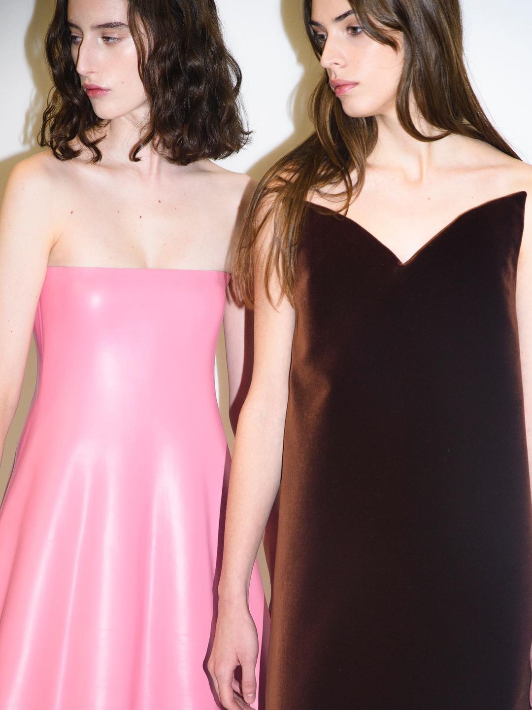 Two models pose in JW Anderson dresses. One in pink and the other in dark brown