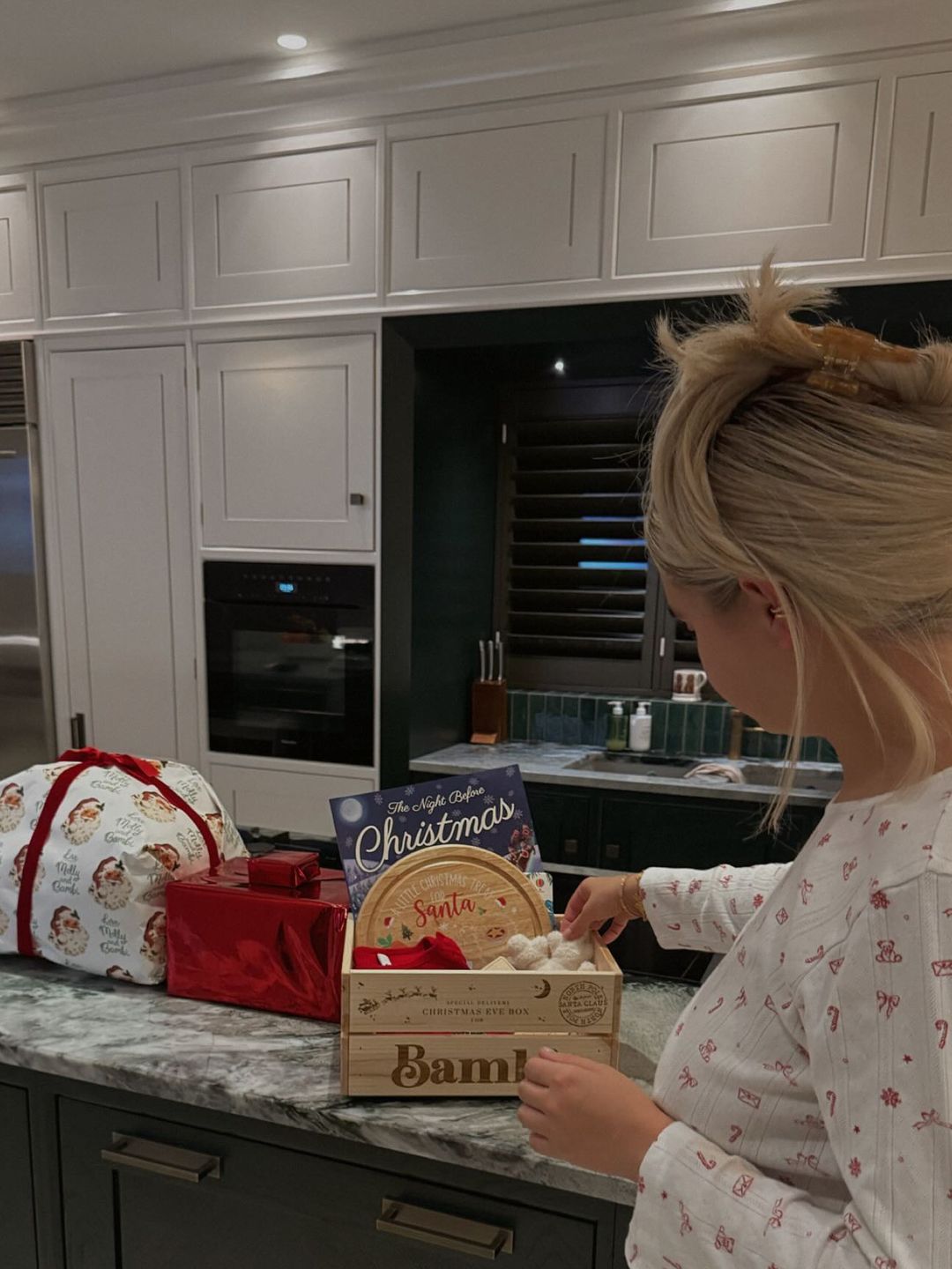 Molly Mae wears white pyjamas with holiday motifs while preparing with a curated Santa box made for a cozy, heartwarming Christmas Eve.