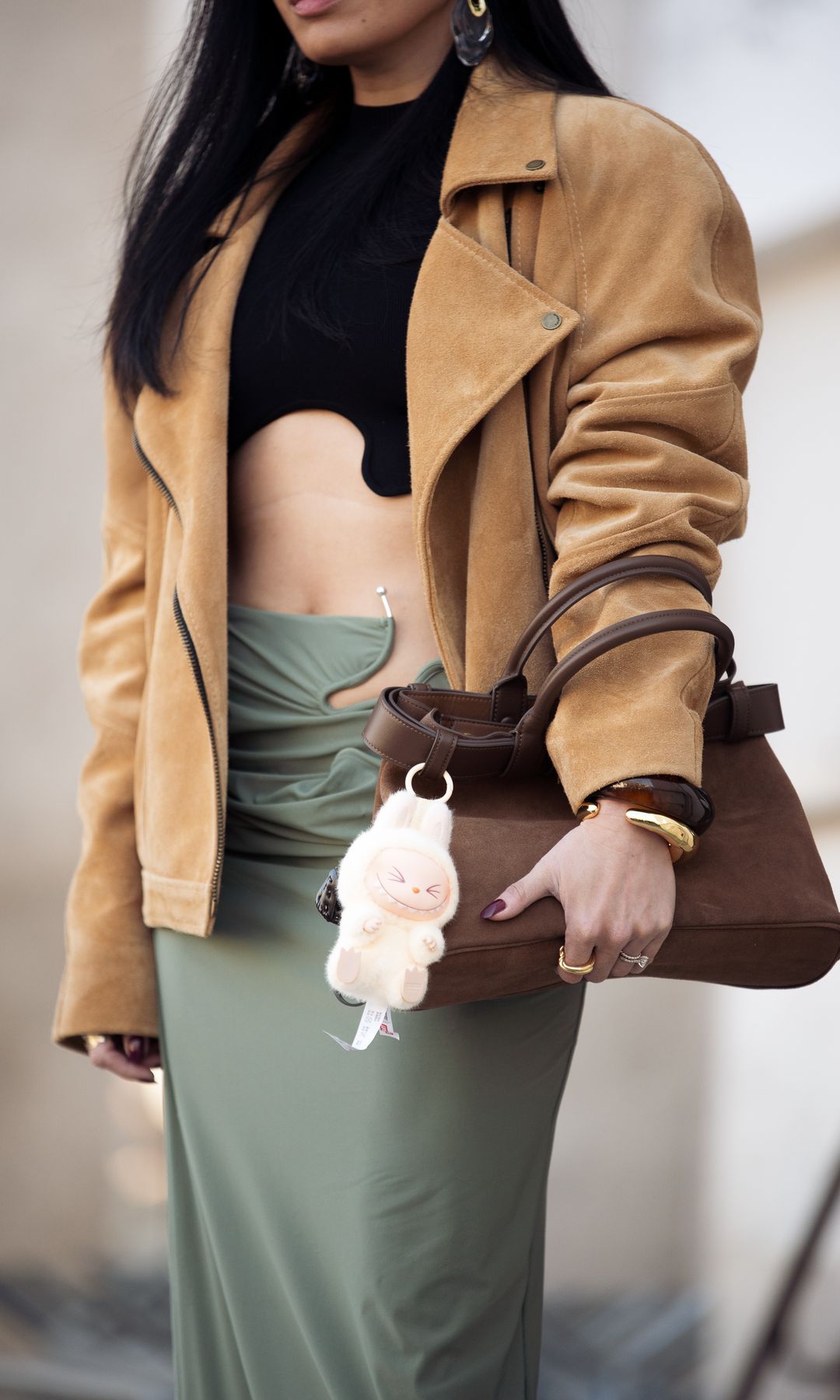 Miki Cheung wears long green pencil skirt with metal details on the waist, black top, beige suede jacket brown bag with a charm and sunglasses outside the Christopher Esber fashion show during the Womenswear Fall/Winter 2025/2026 as part of Paris Fashion Week on March 06, 2025 in Paris, France