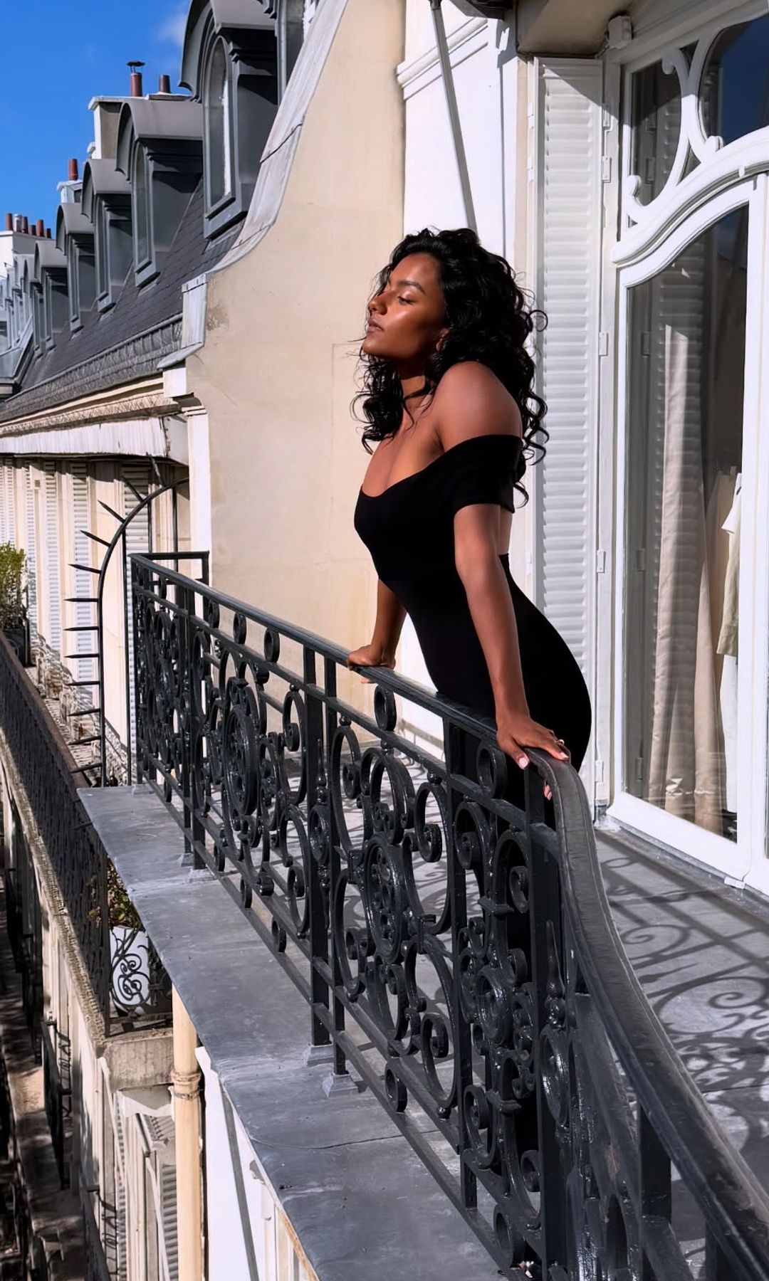 Simone Ashley poses in a black gown on a Paris balcony