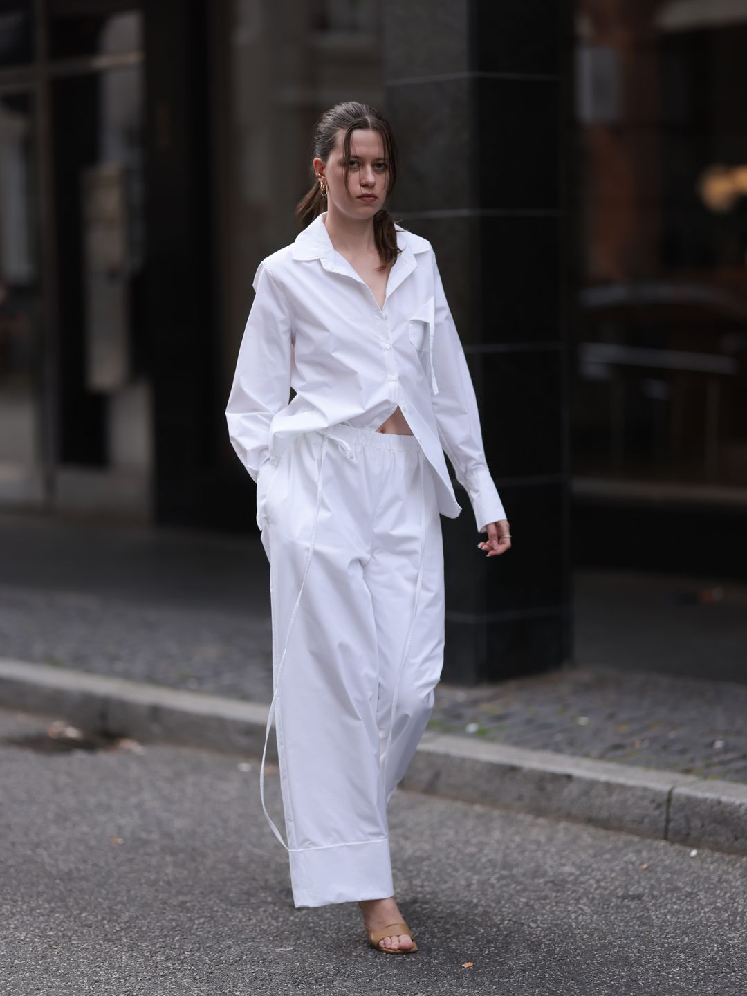 A guest seen wearing gold earrings, Borrensberghs white cotton buttoned blouse and shirt, matching Borrensberghs white cotton long pants and brown leather heels, at the mfpen Store Opening in Copenhagen.