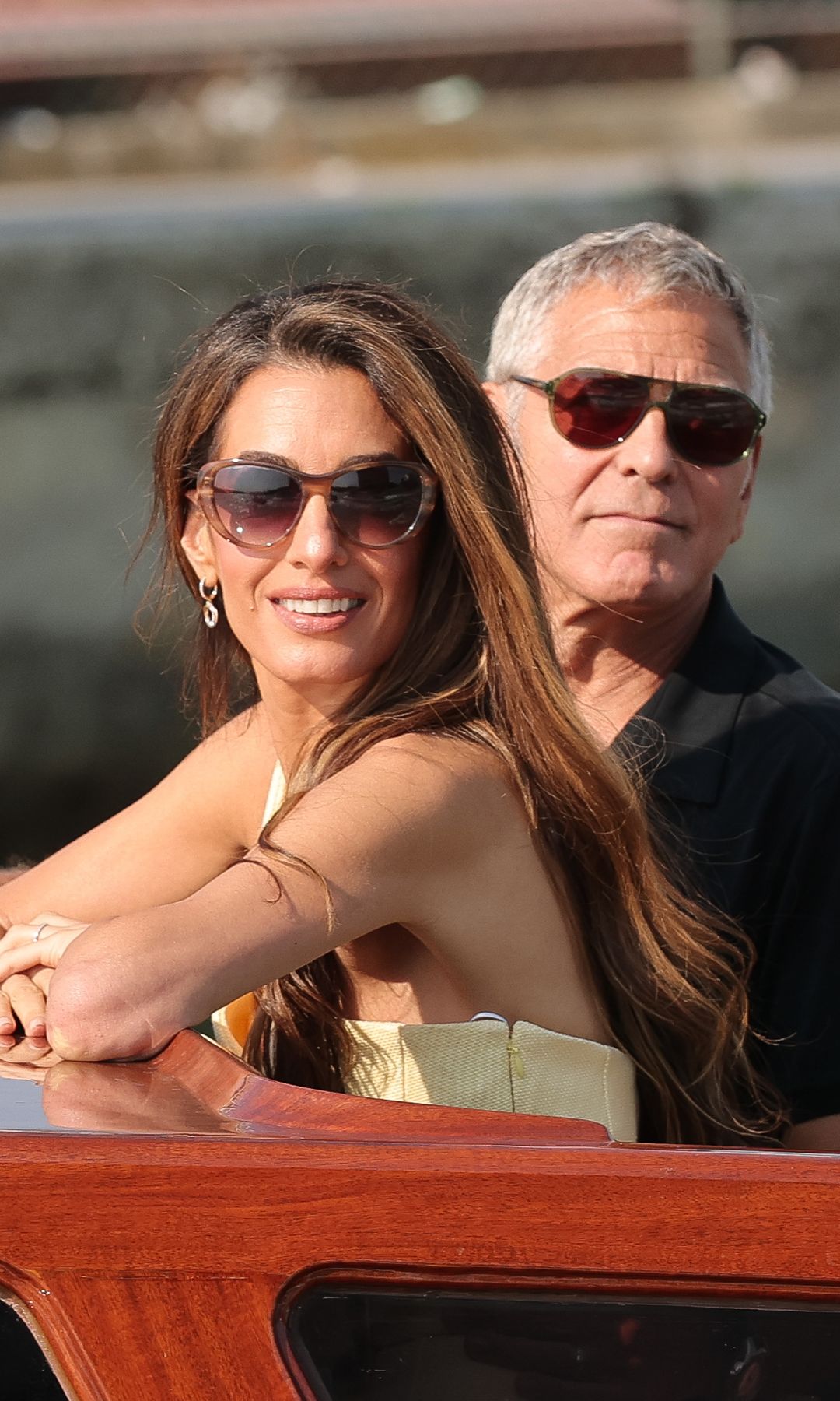 Amal Clooney and George Clooney arriving ahead of the 82nd Venice International Film Festival by boat. Both wear sunglasses and Amal wears a pale yellow dress