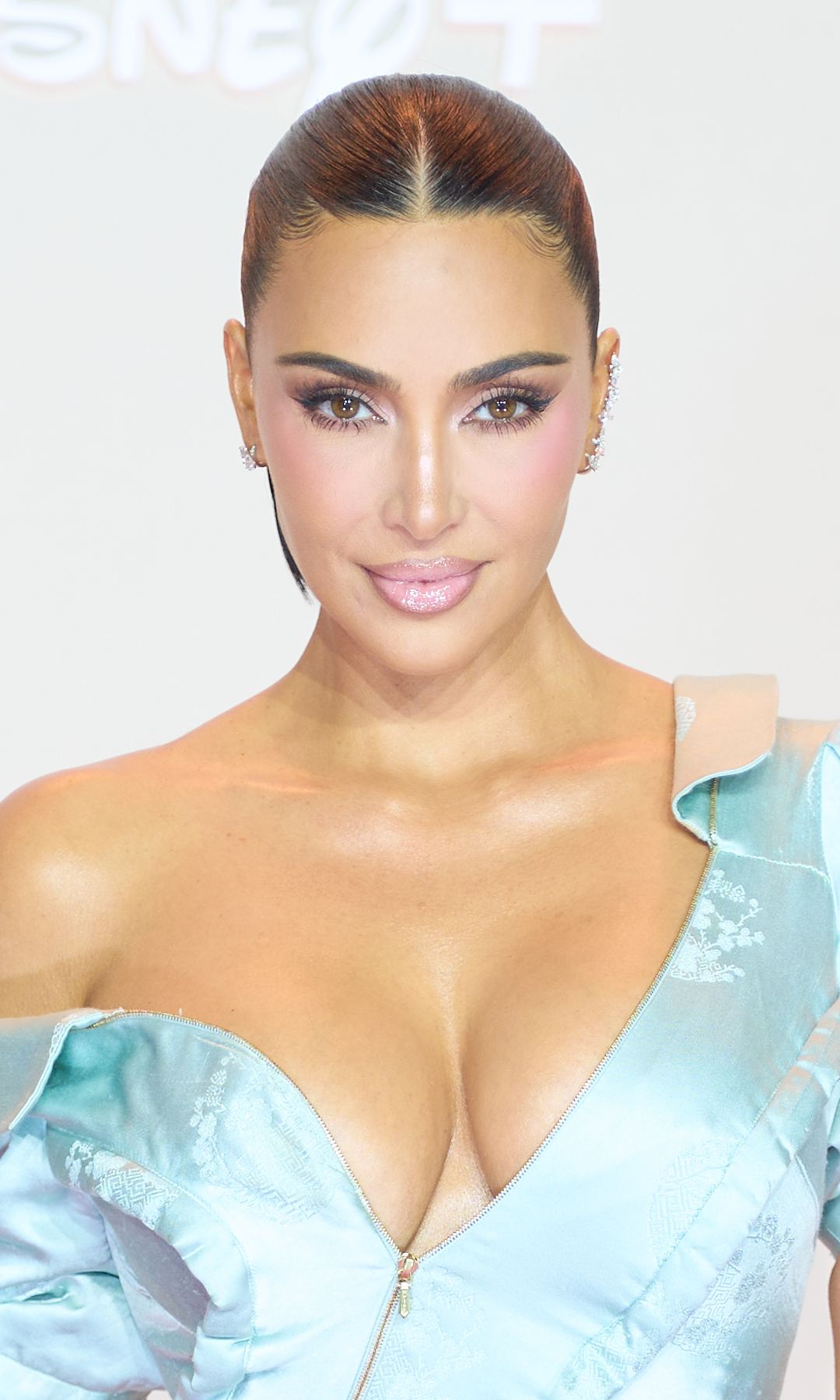 im Kardashian wears a structured off-the-shoulder satin and lustrous maxi gown, low-neck dress by Christian Dior Spring/Summer 2000 collection, in icy blue with sculpted draping, asymmetrical neckline and fitted mermaid silhouette, featuring jacquard floral motifs embroidery and front zipper detail, sleek parted pulled-back hair, jewelry by Repossi, and attends the "All's Fair" Disney+ Premiere at Maison de La Chimie on October 21, 2025 in Paris, France. 