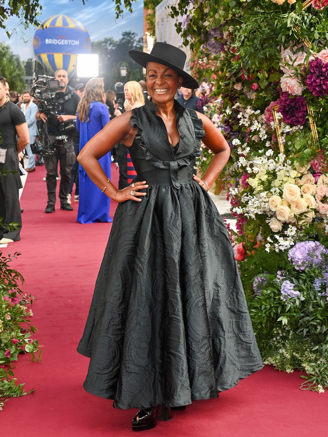 Adjoa Andoh no tapete vermelho com roupa preta e chapéu