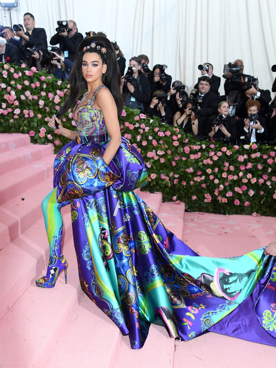 Dua Lipa walking up the pink carpet steps of the met gala in a neon blue and navy Versace patterned gown
