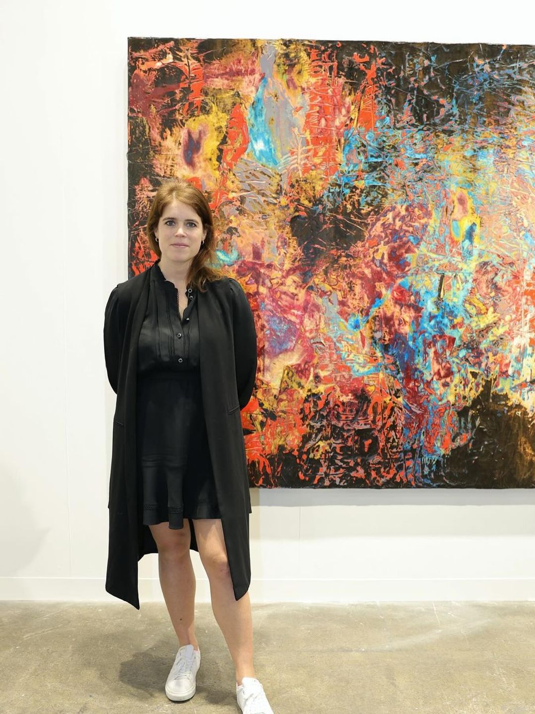 Princess Eugenie poses in a black dress in front of a creative painting