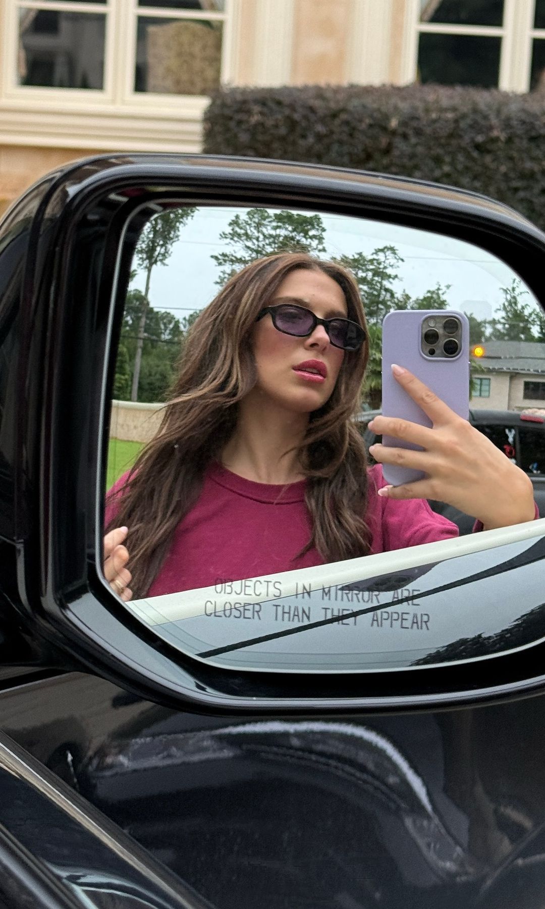 Millie Bobby Brown poses for a photo next to her car, wearing a cherry red co-ord