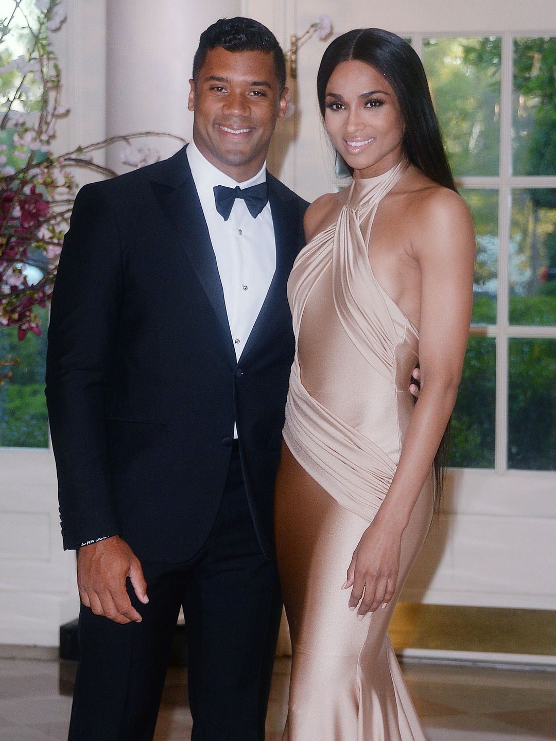 Ciara and Russell smile while wearing black tie attire
