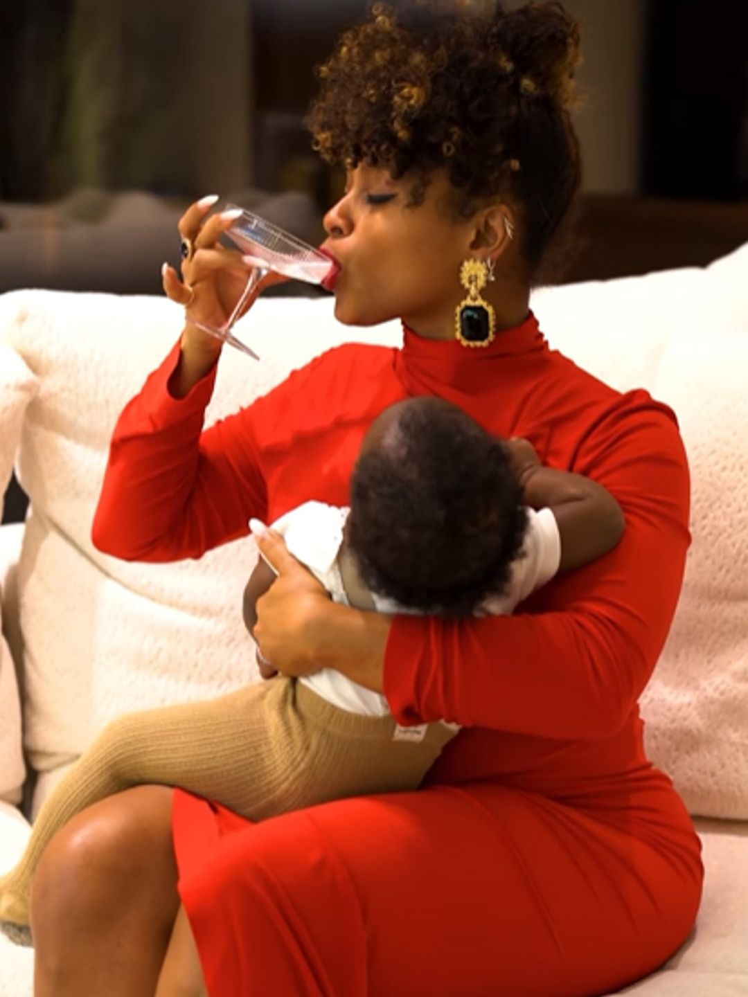 Fleur East drinking a drink with a baby on her lap