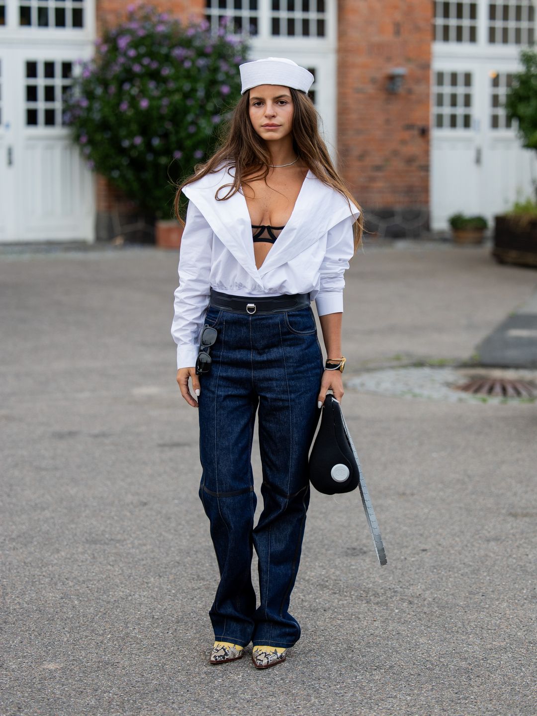 A guest wears white hat, white blouse, blue denim jeans, black bag outside Baum & Pferdgarten during Copenhagen Fashion Week. 