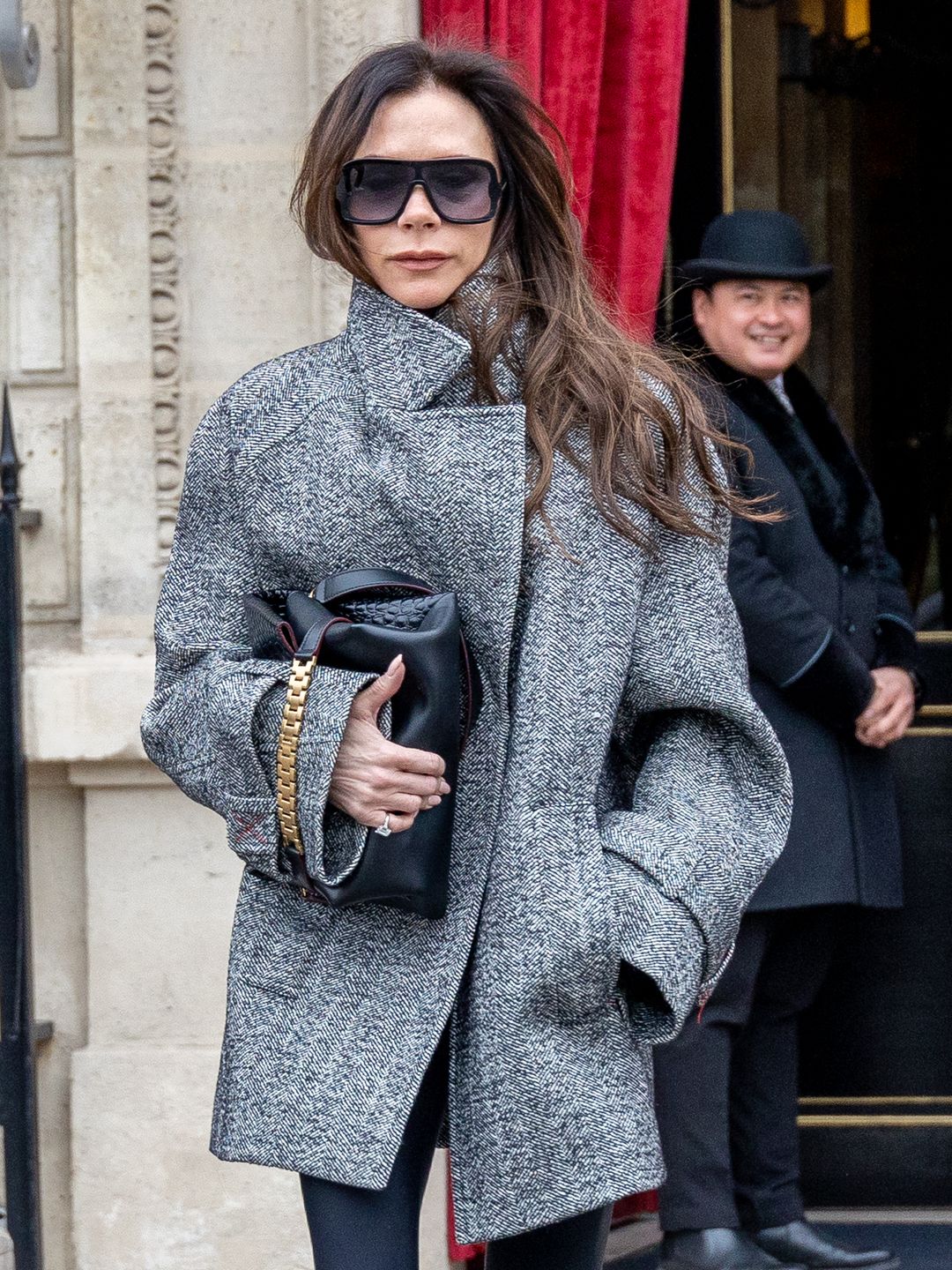 Victoria walking towards the camera in a grey coat, wearing sunglasses