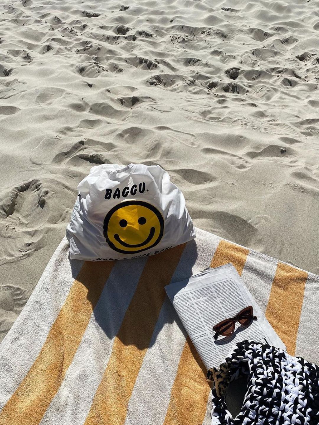 Influencer @julien_xo shares a beachside image of a book, towel and Baggu bag