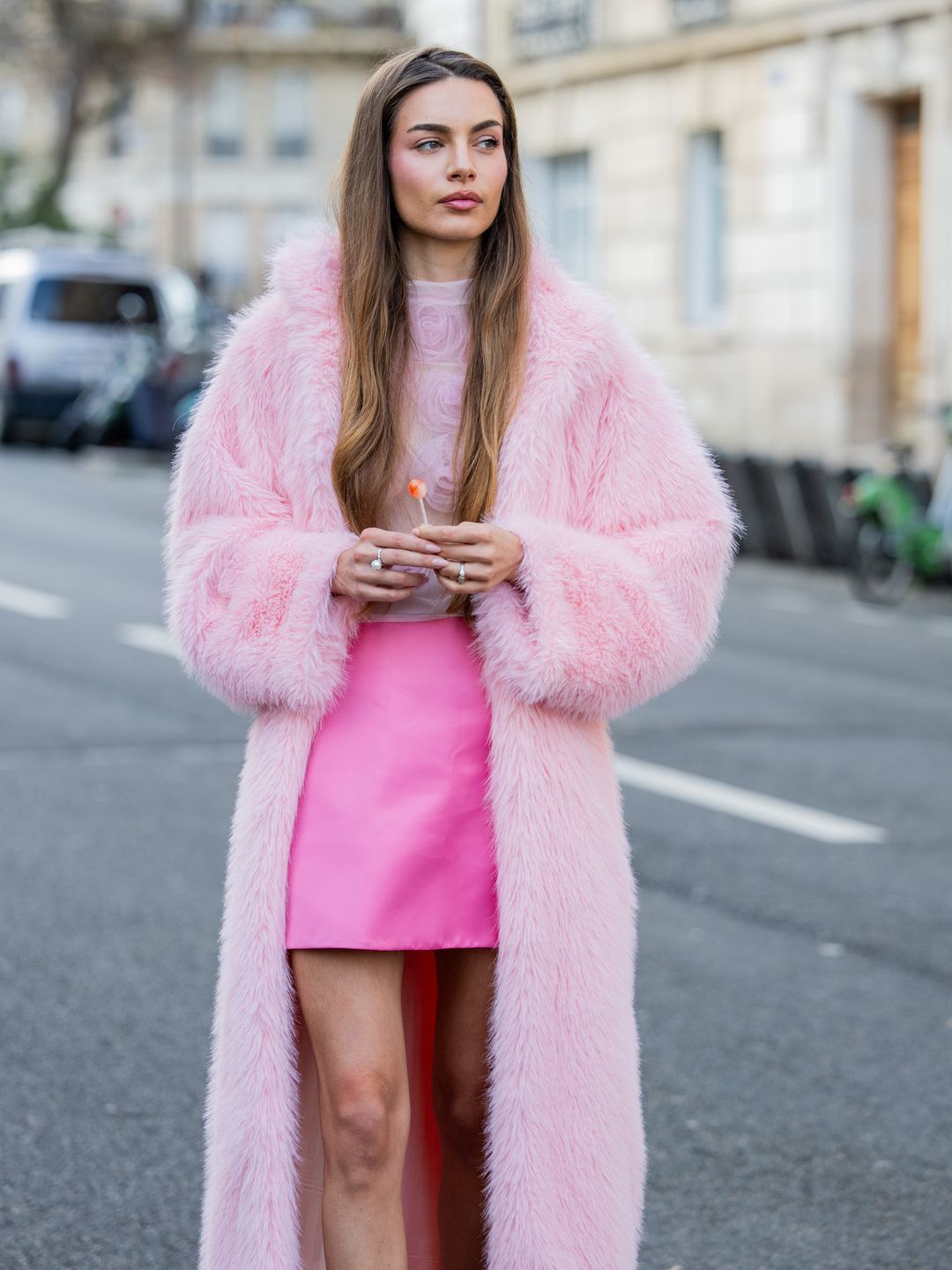 Mara Lafontan with a lollipop wears pink mini skirt, pink faux fur coat, blouse, heels outside Viktor&Rolf during the Haute Couture Spring/Summer 2024