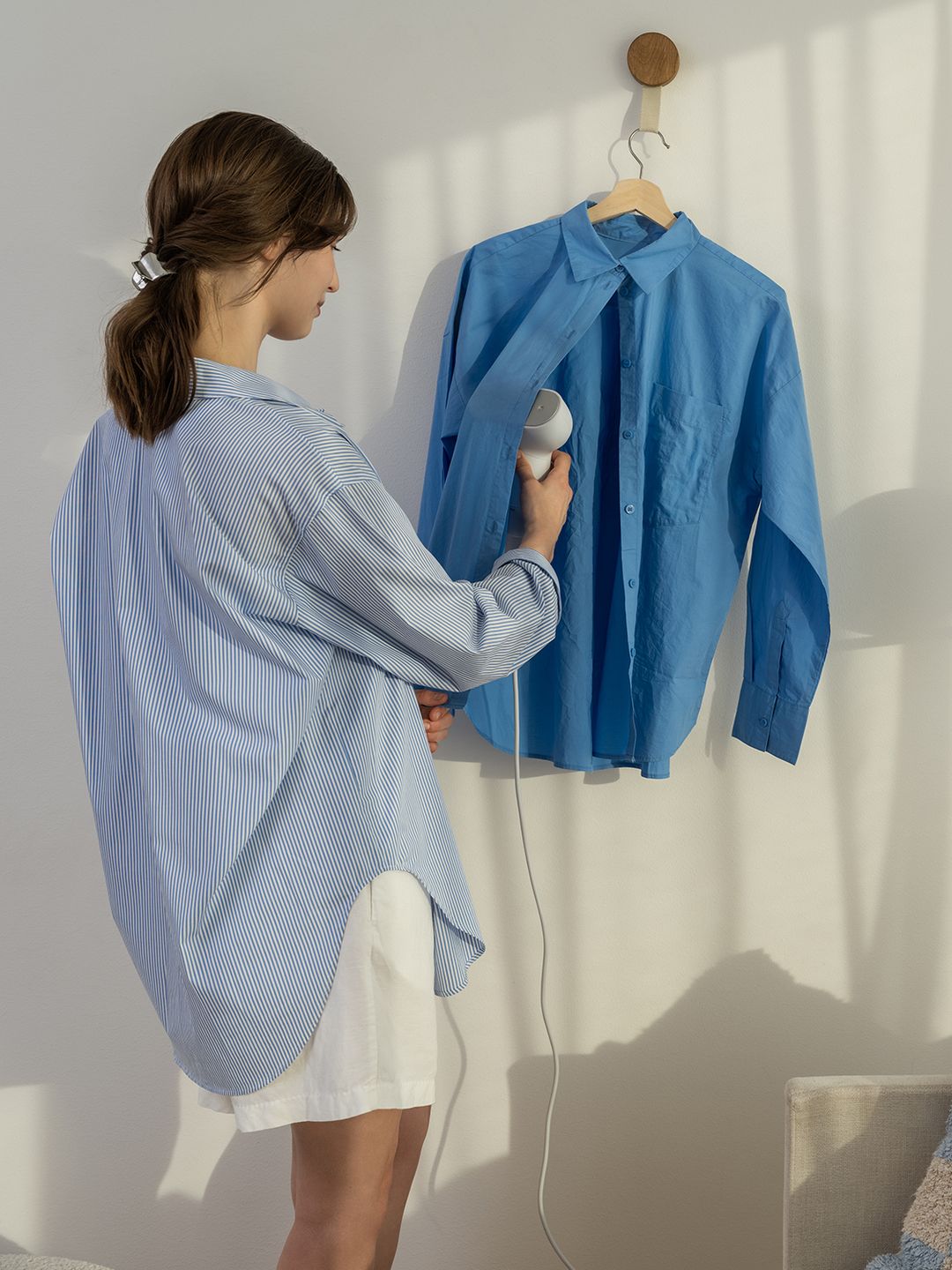 A photo of a woman steaming a blue shirt on a coat hanger 