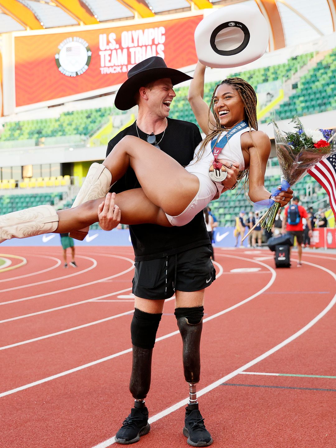 Paralympian Hunter Woodhall holding his girlfriend Tara Davis in his arms as she raises a cowboy hat 