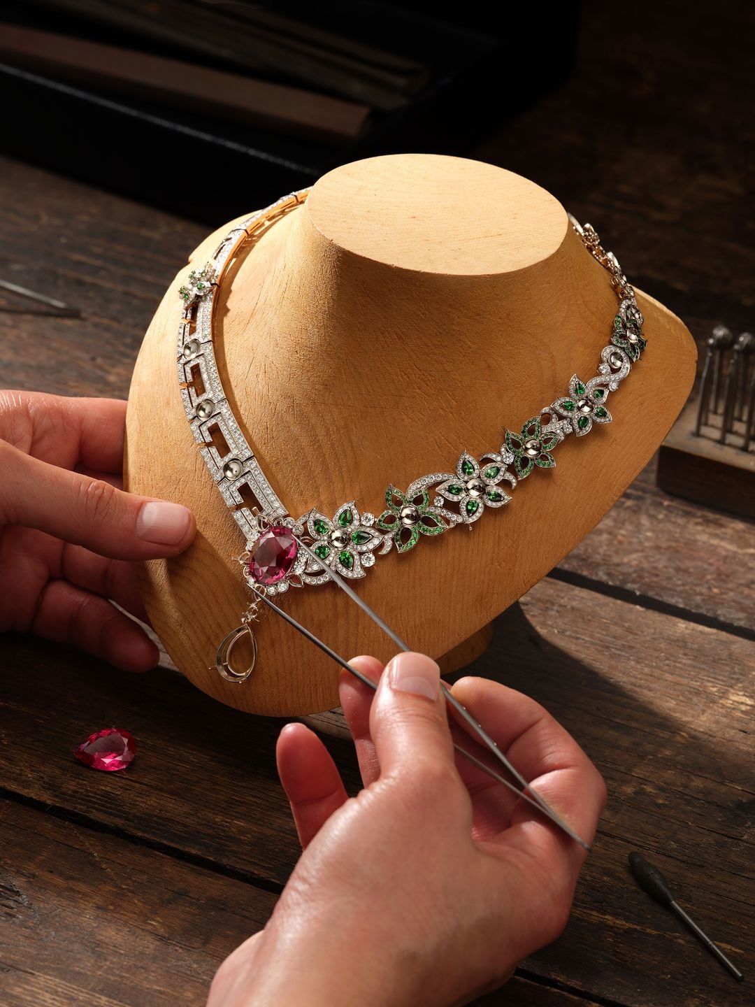 A jeweller adds the finishing touches to a necklace which features pink and green gemstones