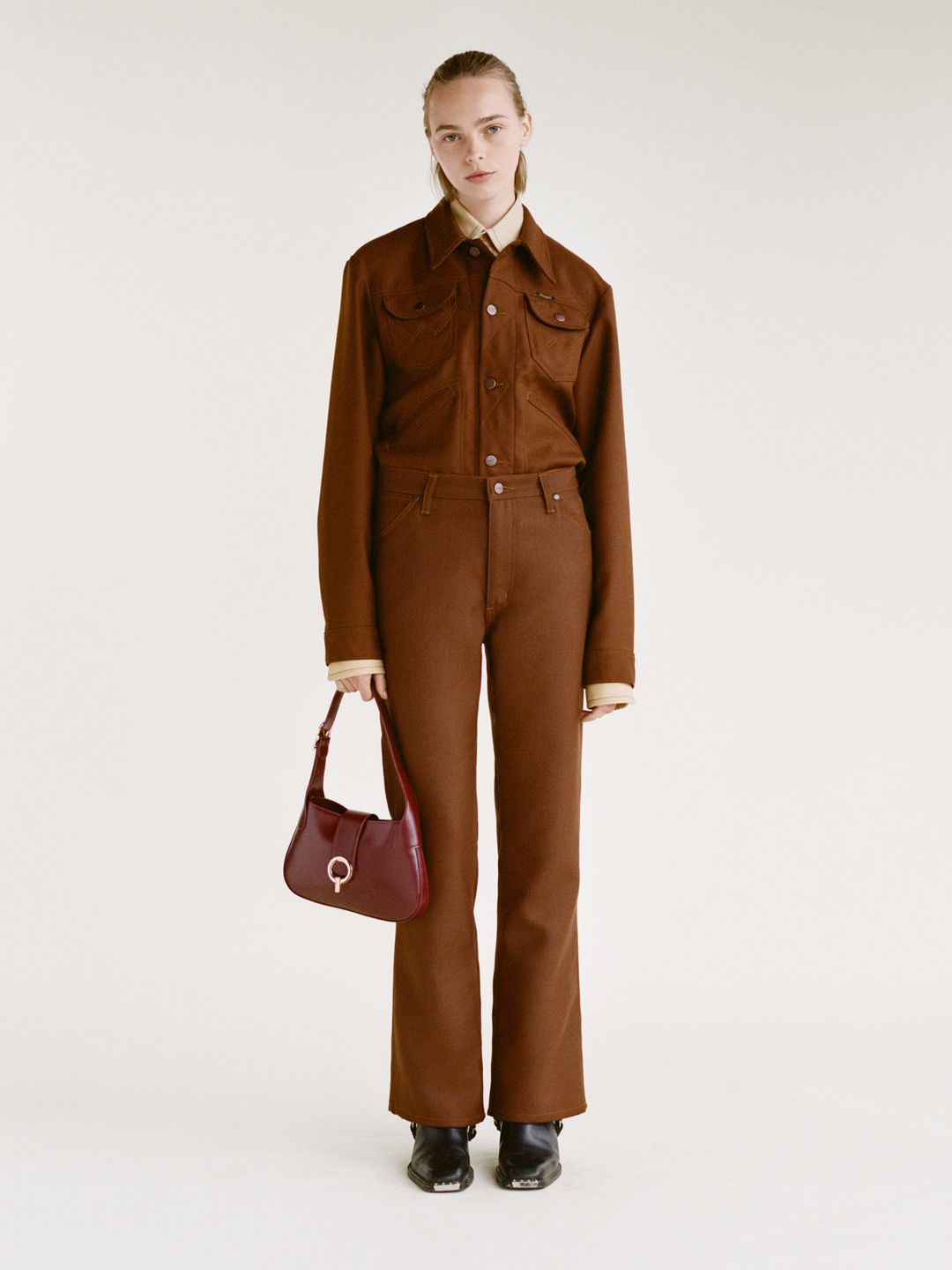 Model in brown denim jacket and jeans with red shoulder bag 