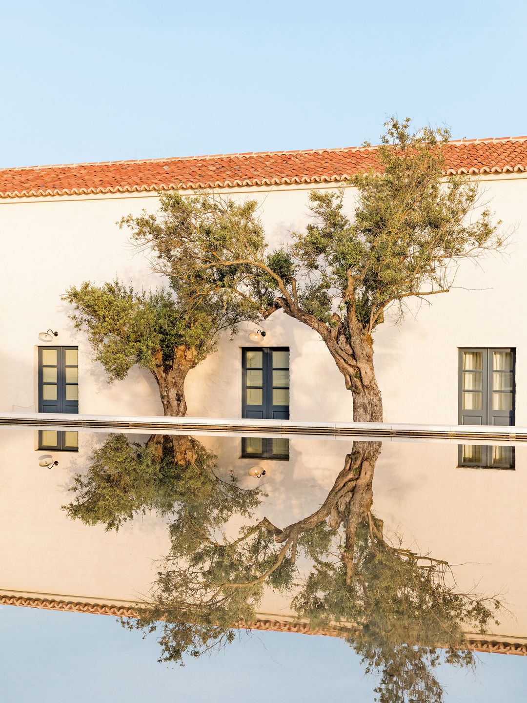 A serene scene of a white building with terracotta roofing, reflected in a still water surface.