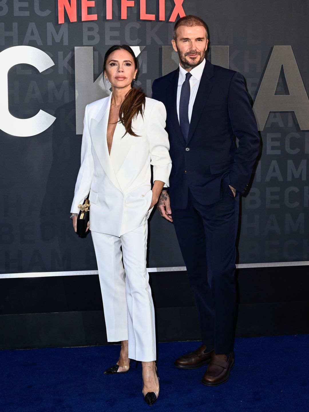 Victoria and David Beckham pose on the red carpet for the Netflix 'Beckham' UK Premiere. Victoria sports a white suit and David a navy blue.
