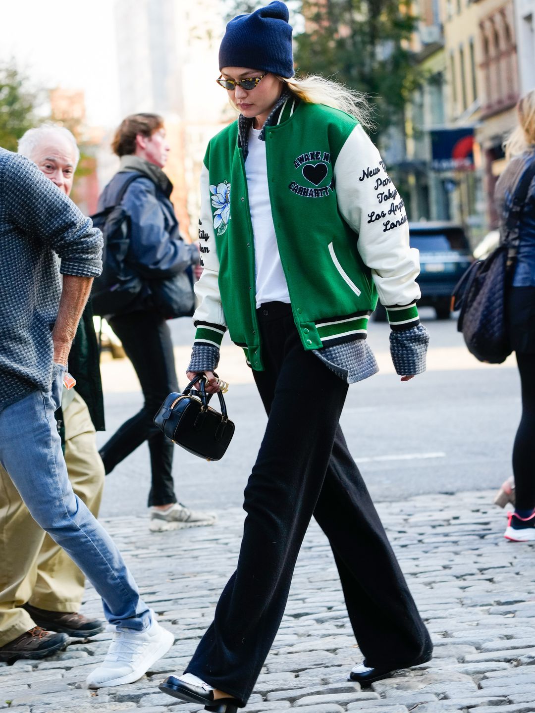 Gigi Hadid is seen on November 05, 2023 in New York City wearing a navy blue beanie, green and white varsity jacket and black pants