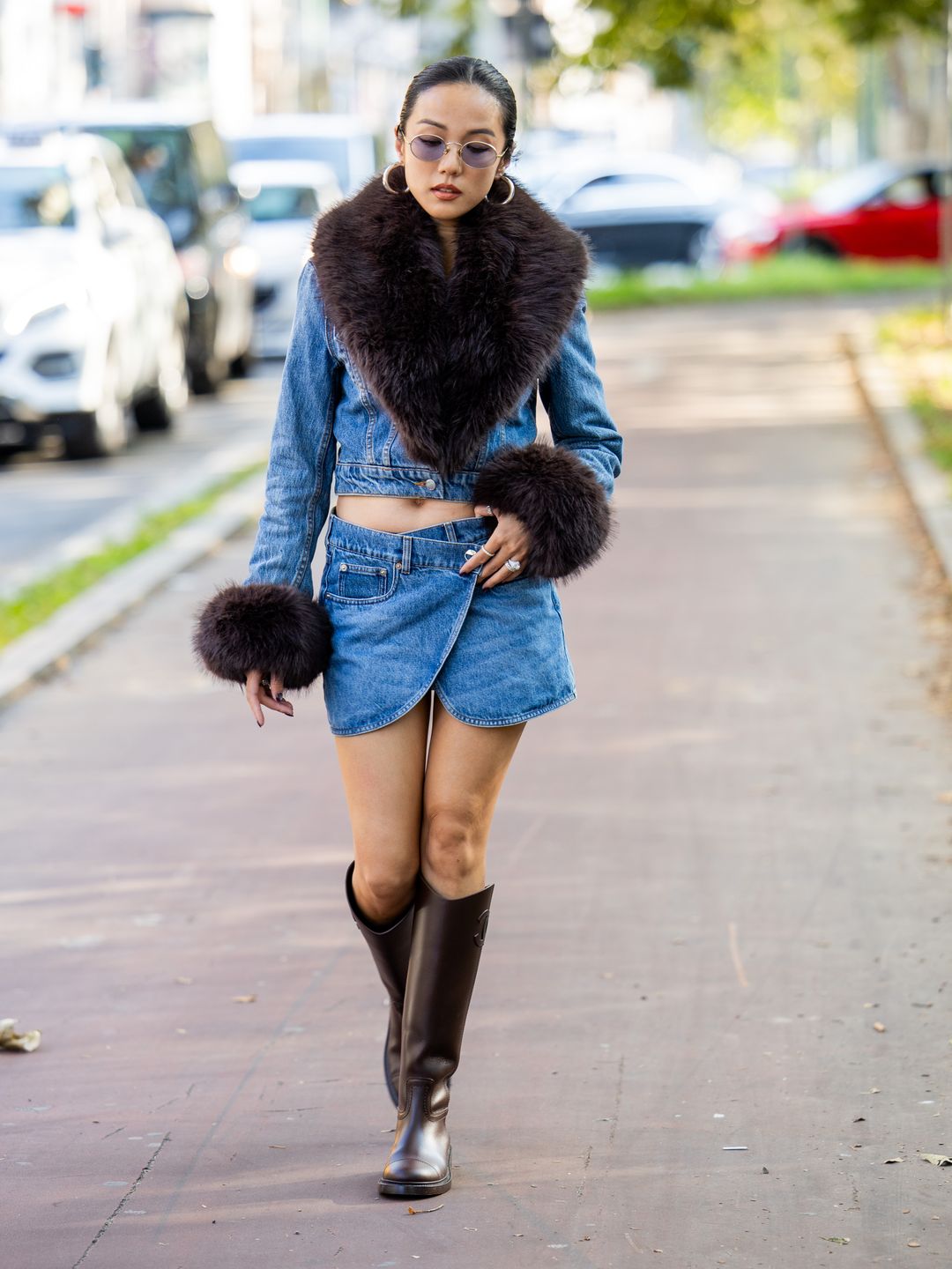 Yoyo Cao wears denim wrapped skirt, shirt with brown fur collar sleeves, sunglasses, brown boots outside The Attico d