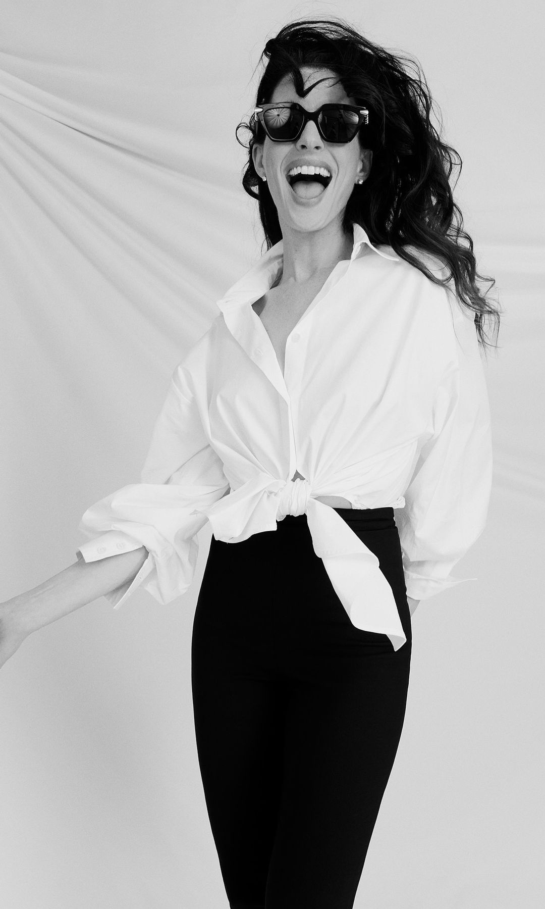 Anne Hathaway poses for a picture in a white button-up shirt and black capri pants in a black and white image on her Instagram