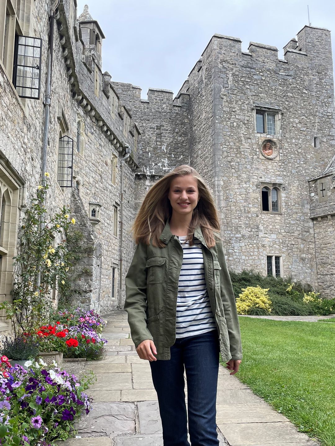 Princess Leonor in a green jacket, striped shirt and denim jeans walking between stone buildings