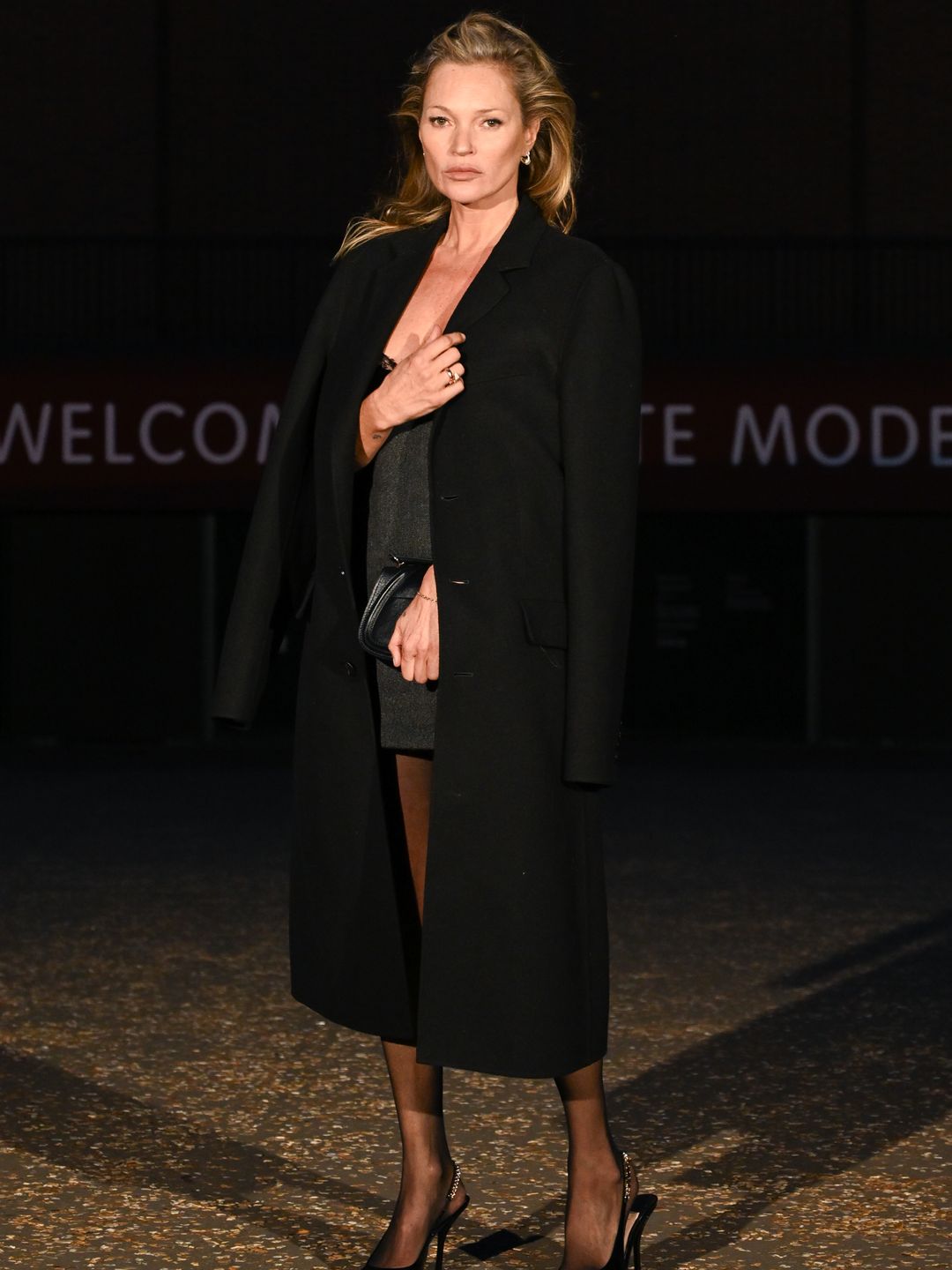 Kate Moss wearing a black coat over a grey mini dress 