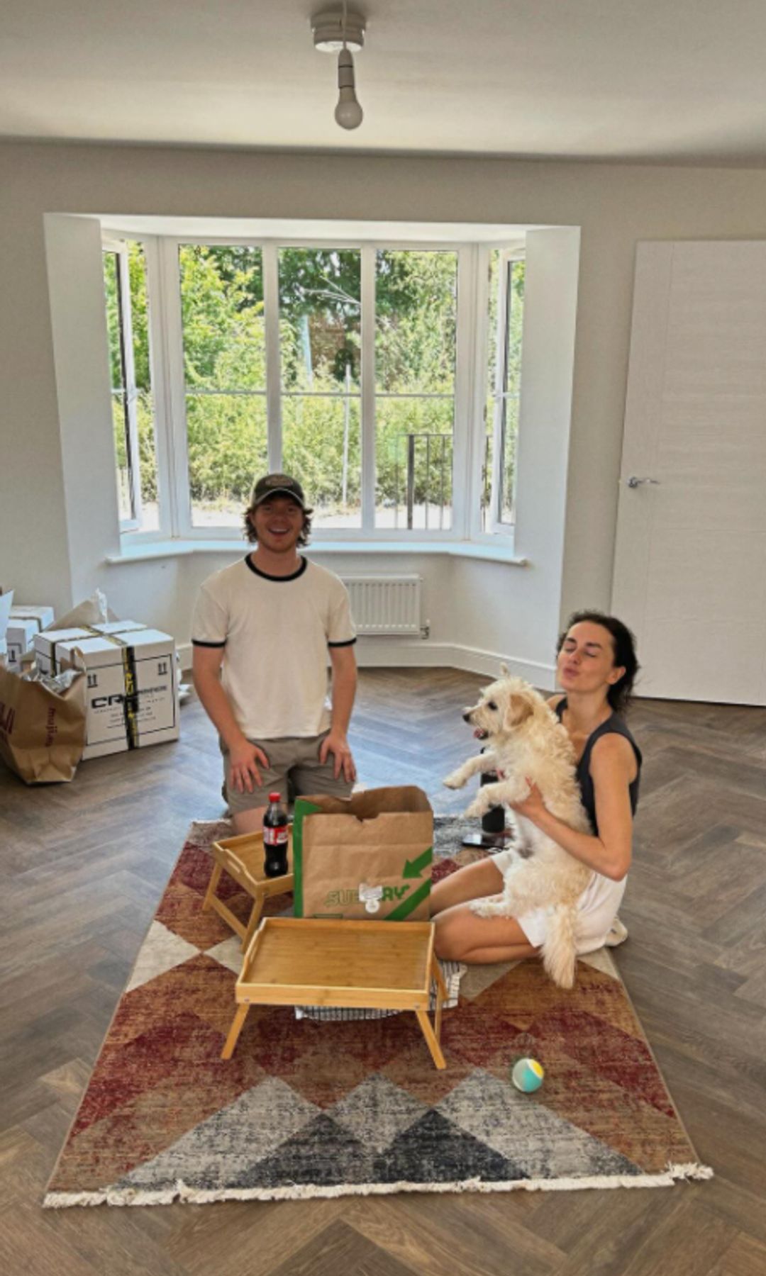 Amber Davies and her boyfriend Ben Jouce in a mostly unfurnished living room looking out onto a garden