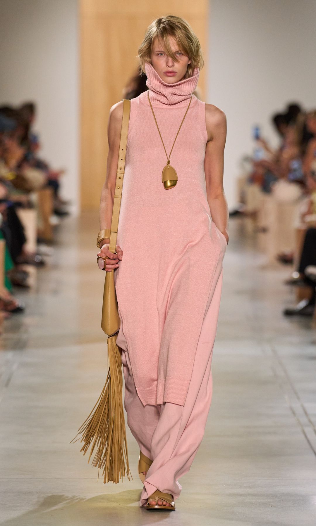 A model wears a pale pink knitted polo neck tunic with matching trousers and taupe accessories