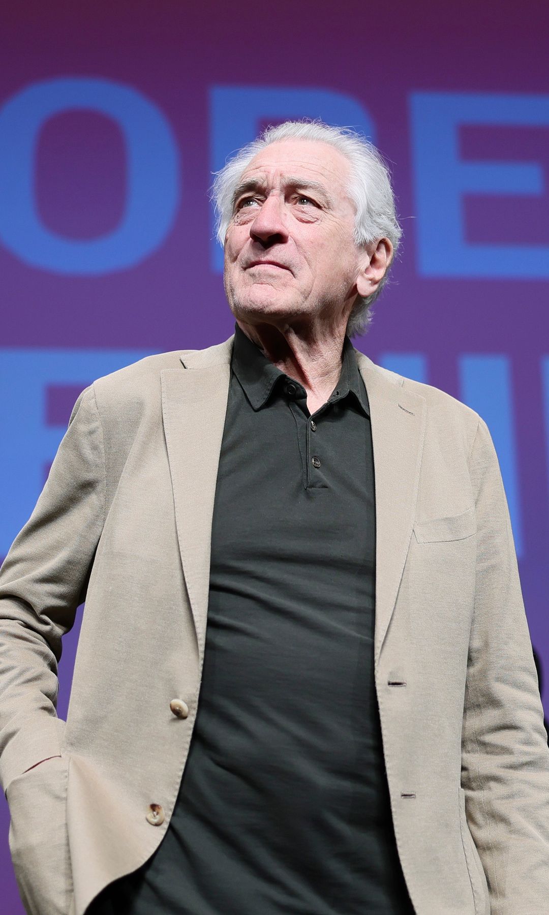 Robert De Niro in a tan suit in front of a sign with his name on it