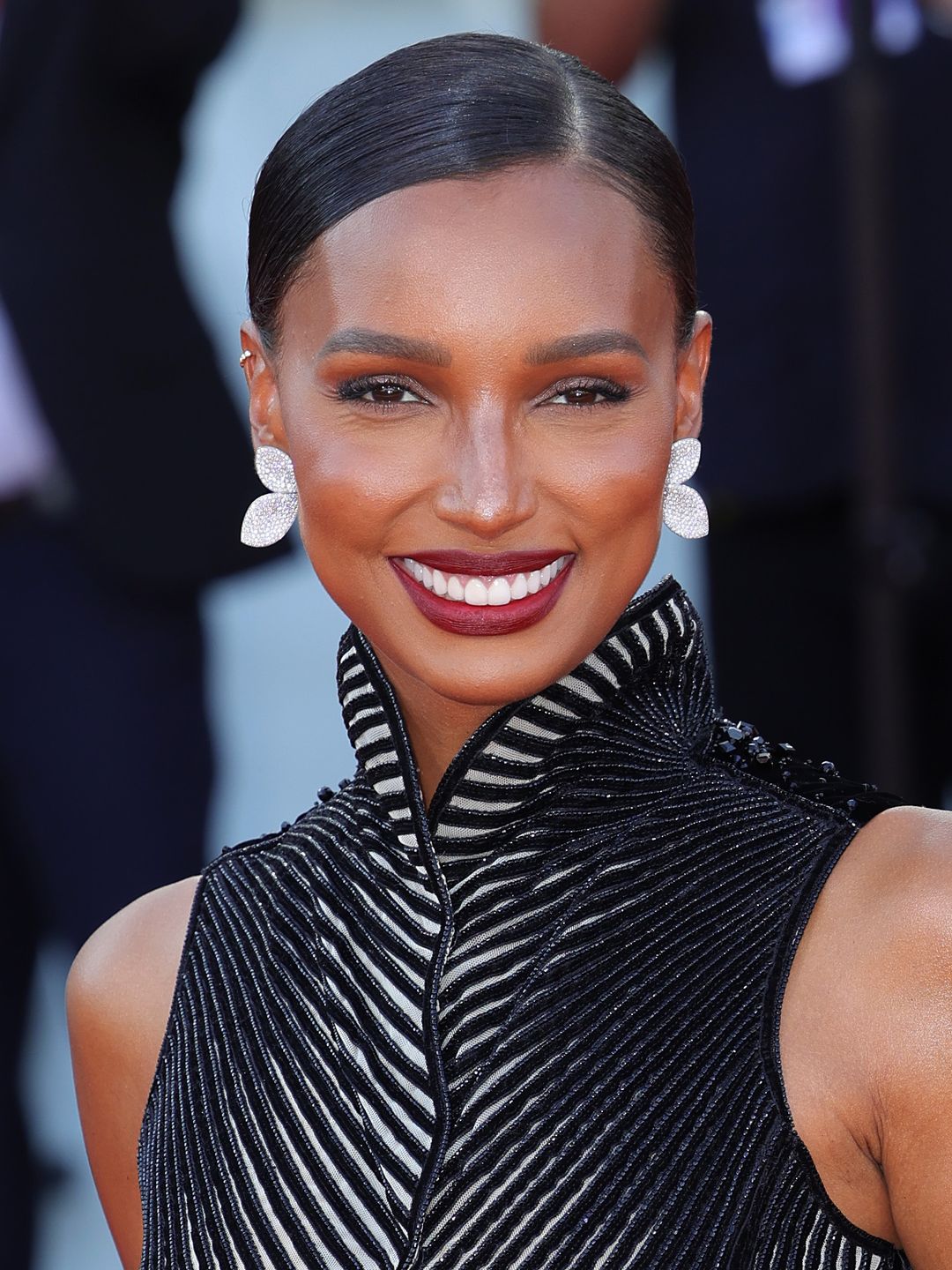 Jasmine Tookes wears a deep plum lipstick and slicked back hairstyle 