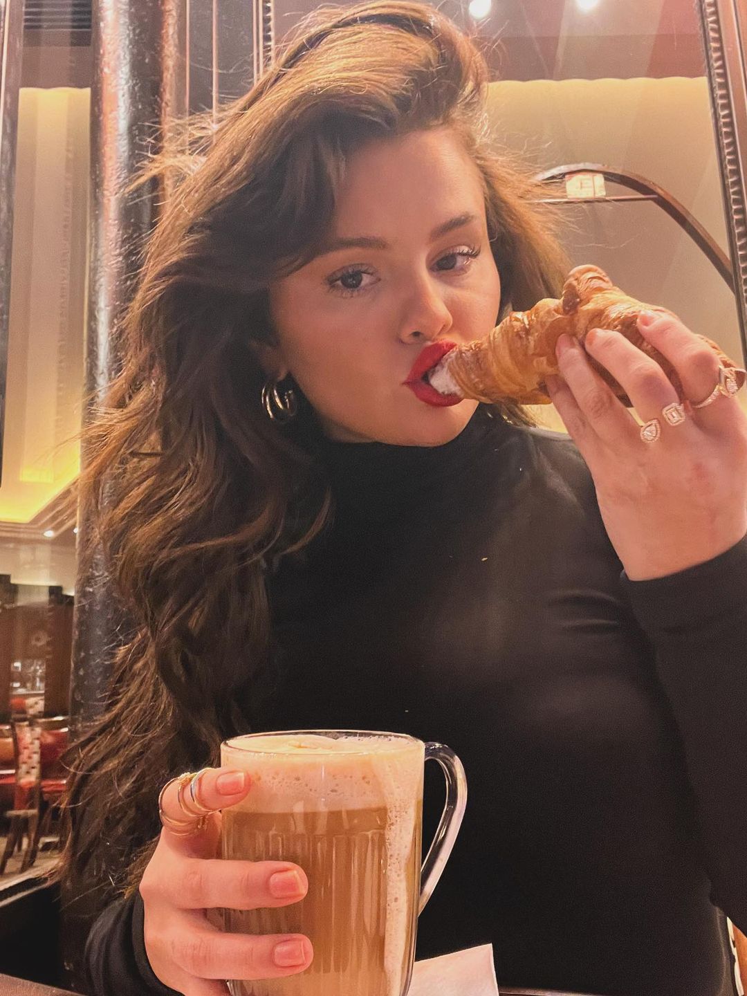 Selena Gomez eats a croissant in Paris wearing a black turtleneck and red lip