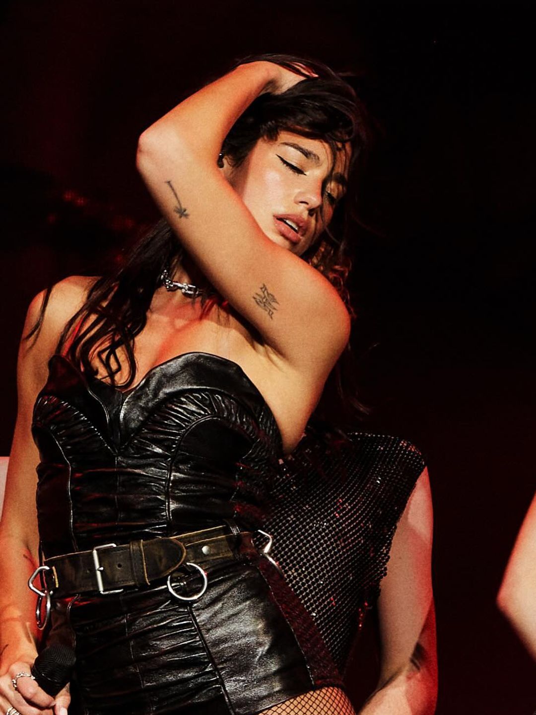 Dua Lipa poses on stage in a leather bodysuit and fishnet tights