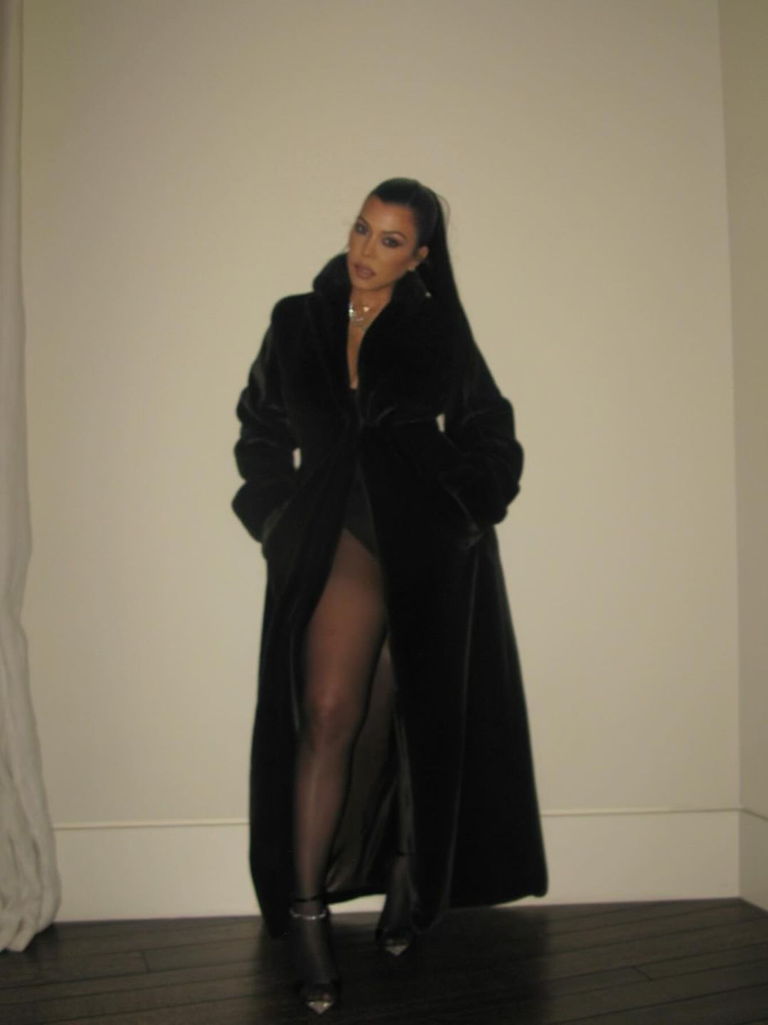 Kourtney Kardashian wearing a black leotard and coat. 