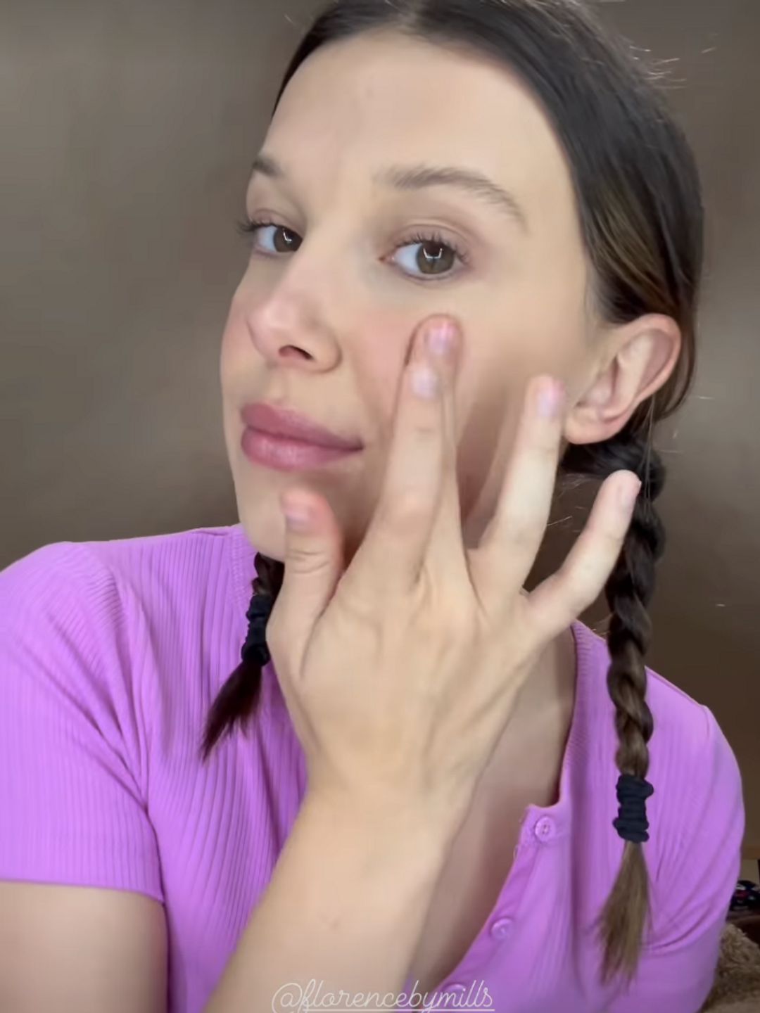 Millie Bobby Brown applying cream blush to the apples of her cheeks 