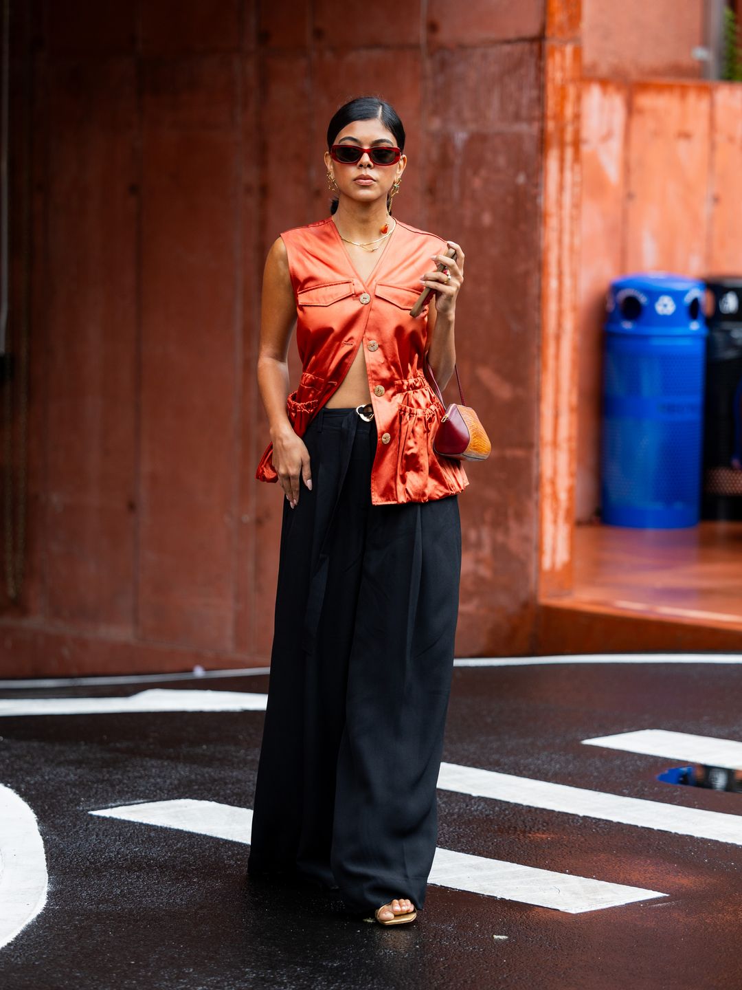 A New York Fashion Week guest styles an orange waistcoat alongside fluid, dark trousers