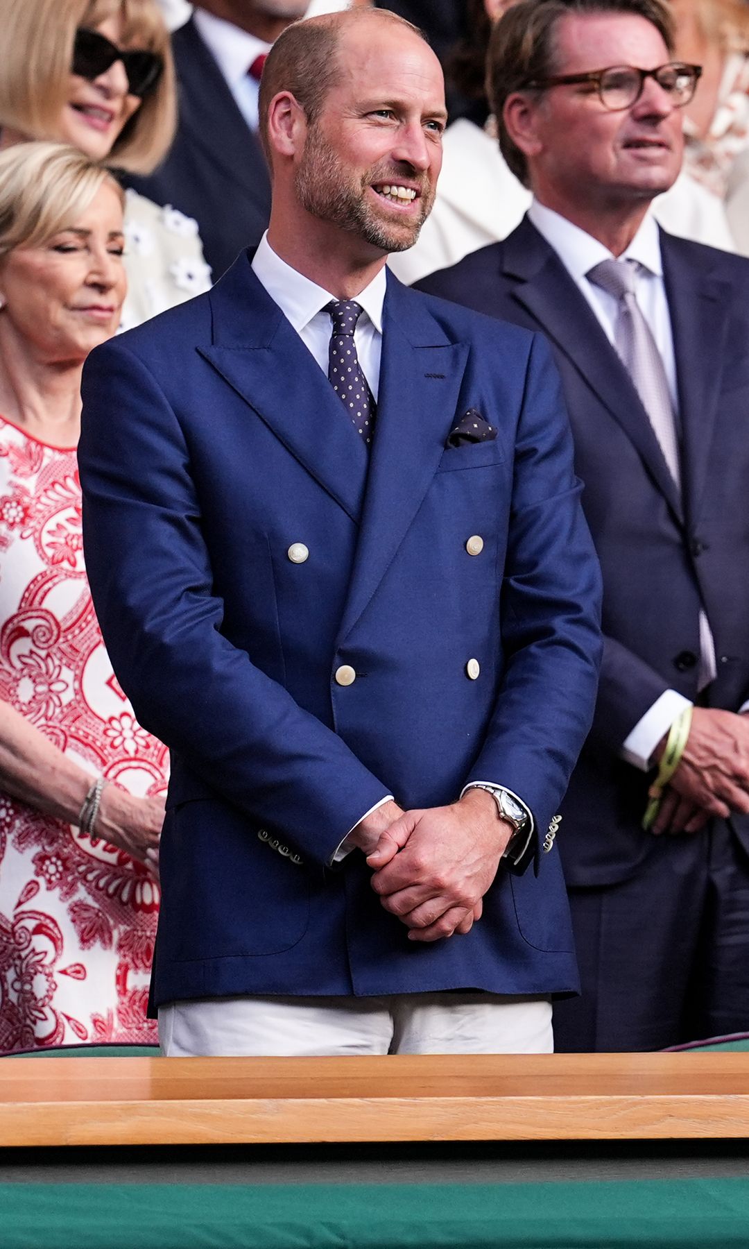 Prince William smiling and clasping his hands next to Prince George