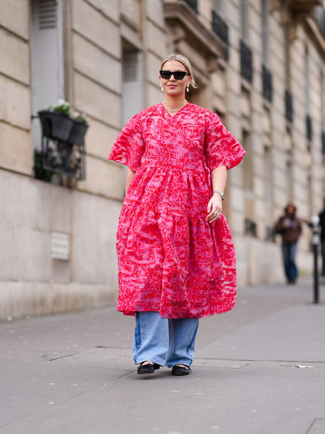 A guest wears sunglasses, a pink floral print oversized gathered / pleated midi dress , a JW Anderson leather bag, blue wide-leg flared denim jeans, outside Cecilie Bahnsen,